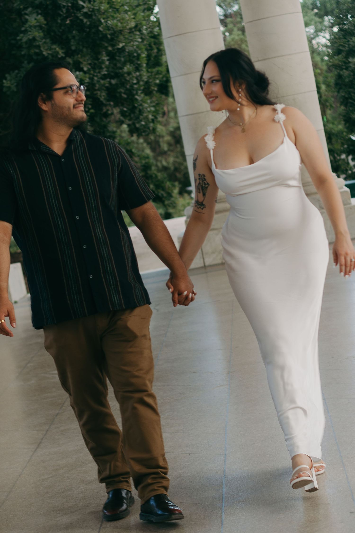 Couple walking hand in hand along a columned walkway.