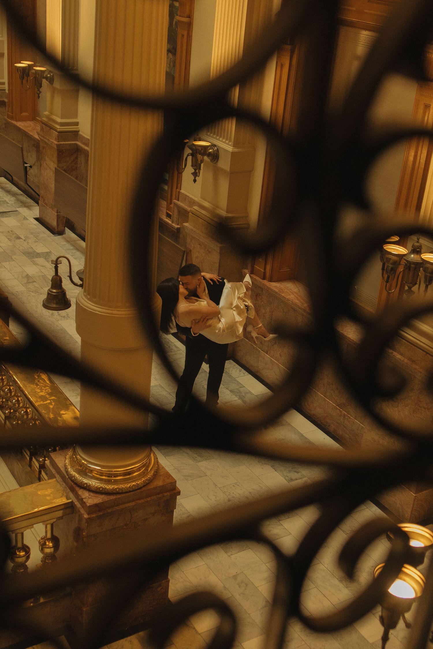 Looking down through ornate metalwork at a warmly lit classical interior with wooden furnishings.