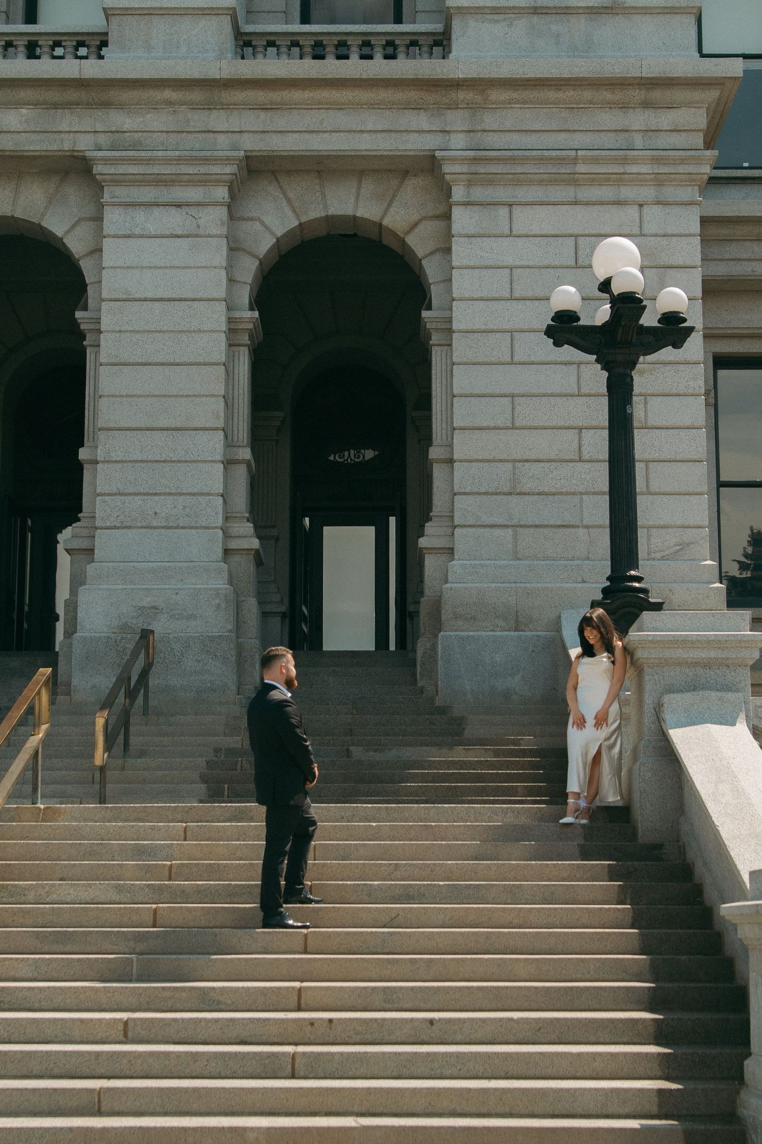 Two people standing on elegant stone steps outside a classic building entrance with ornate light post and arched columns.