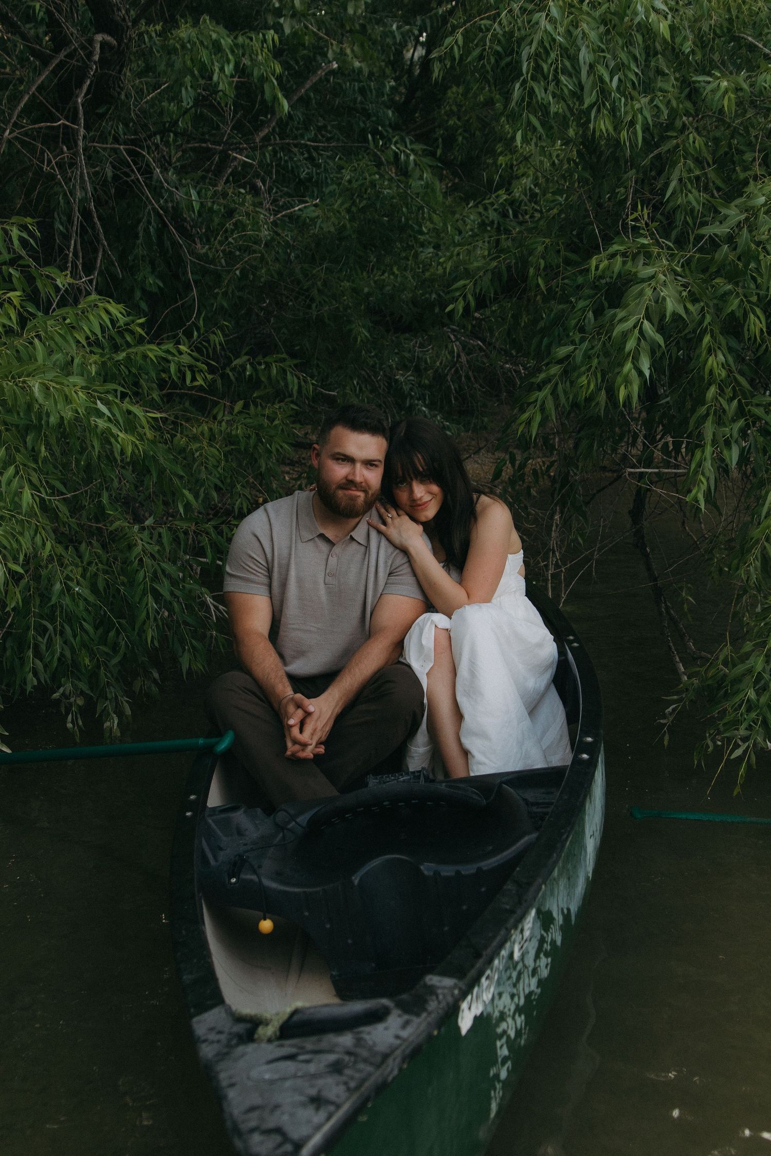 A tender moment shared between two people in a canoe surrounded by green willow branches.