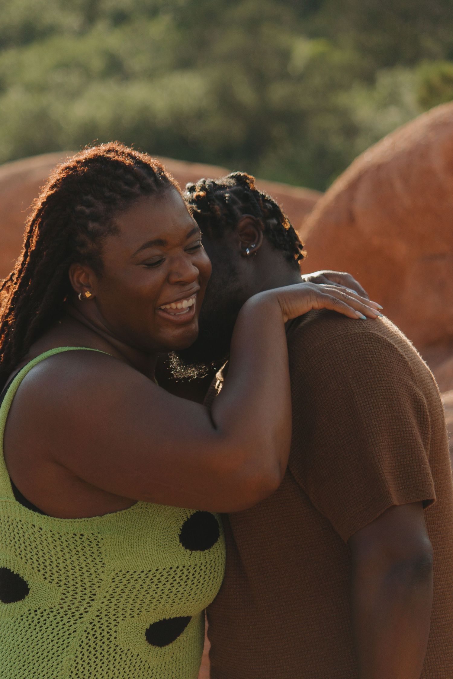 A couple embraces in warm sunlight wearing a lime green polka dot dress and brown clothing.