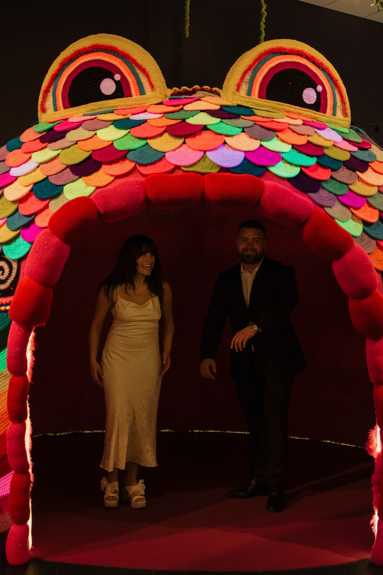 Colorful rainbow-like arch structure with sequined panels illuminated against a dark background on stage.