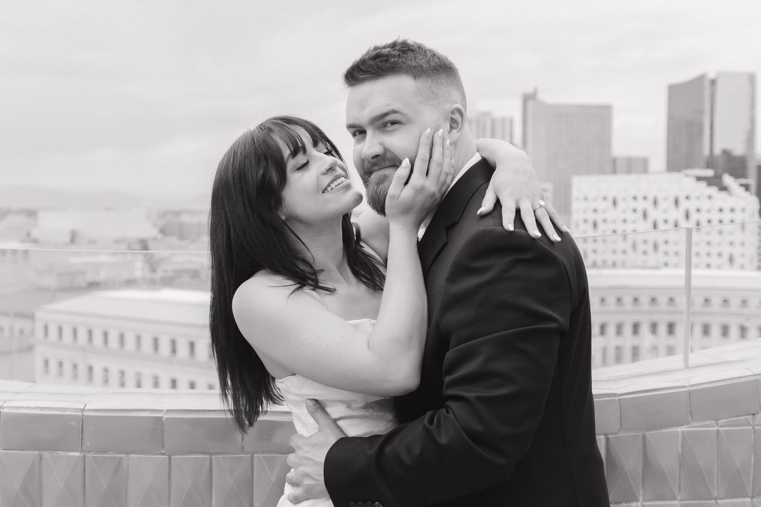 A couple embraces against an urban rooftop backdrop in black and white.