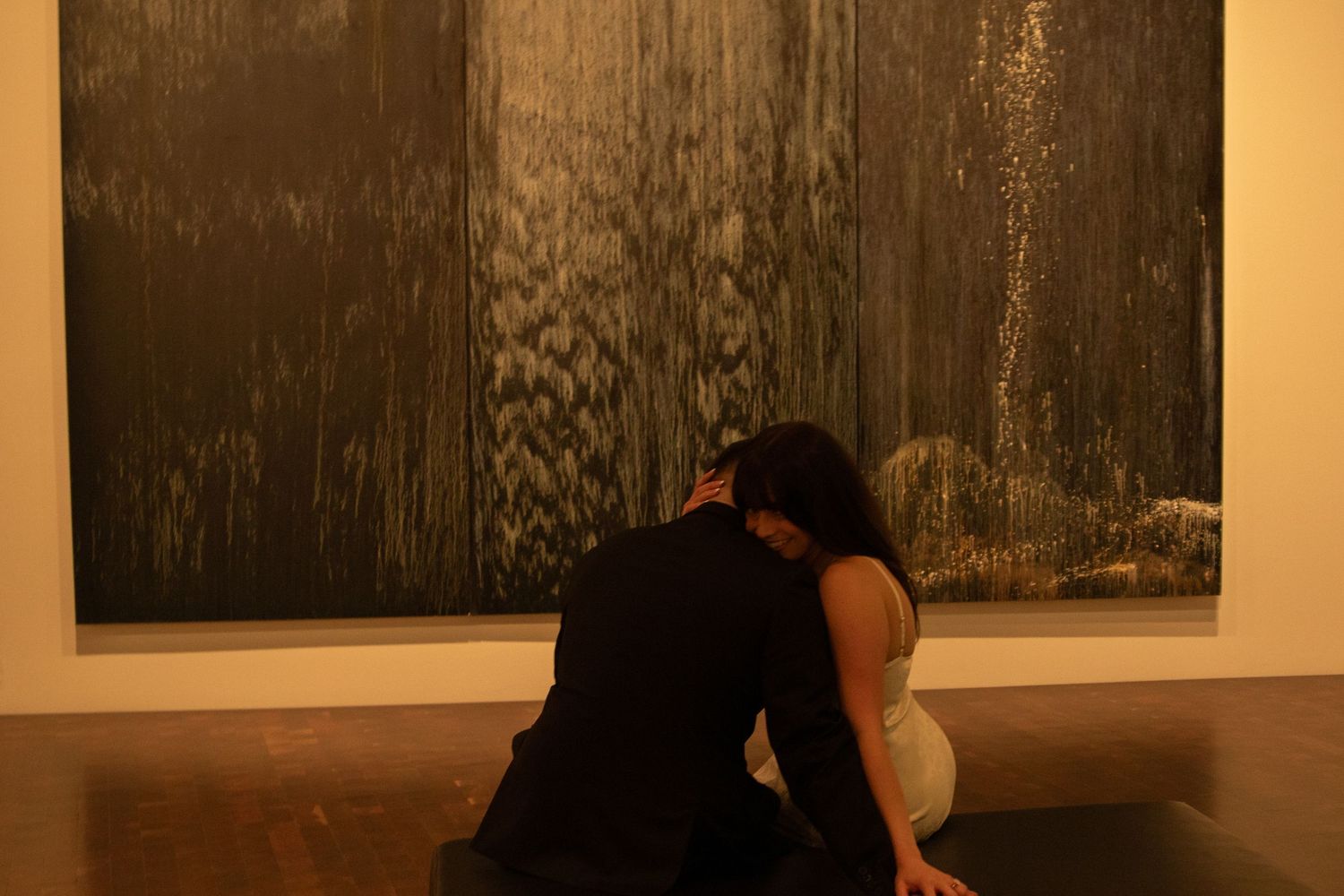 Series of dark monochromatic photographs displayed on gallery wall with viewer silhouette.