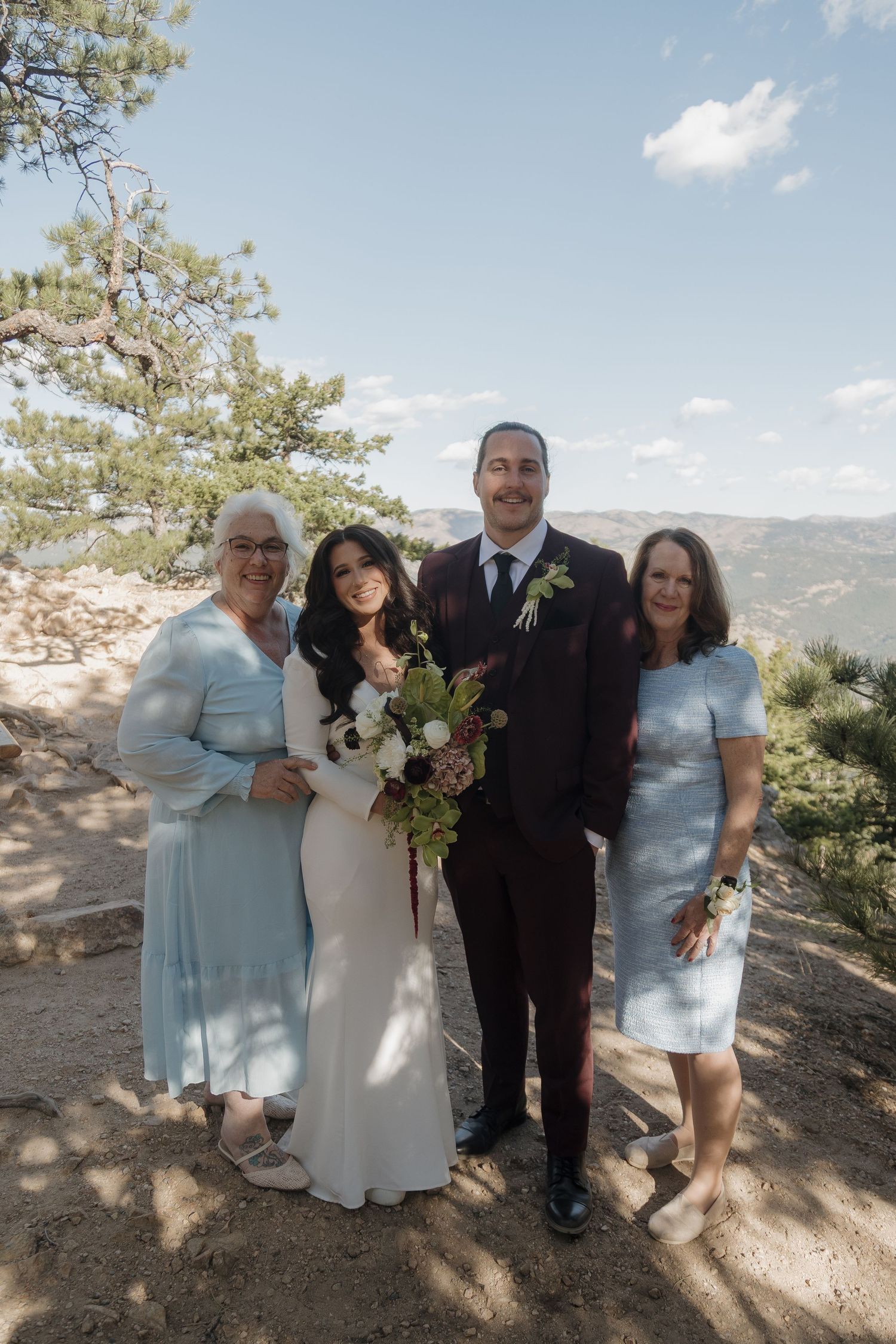 Wedding party group photo outdoors on mountain overlook, bride and groom with two women in light blue dresses.