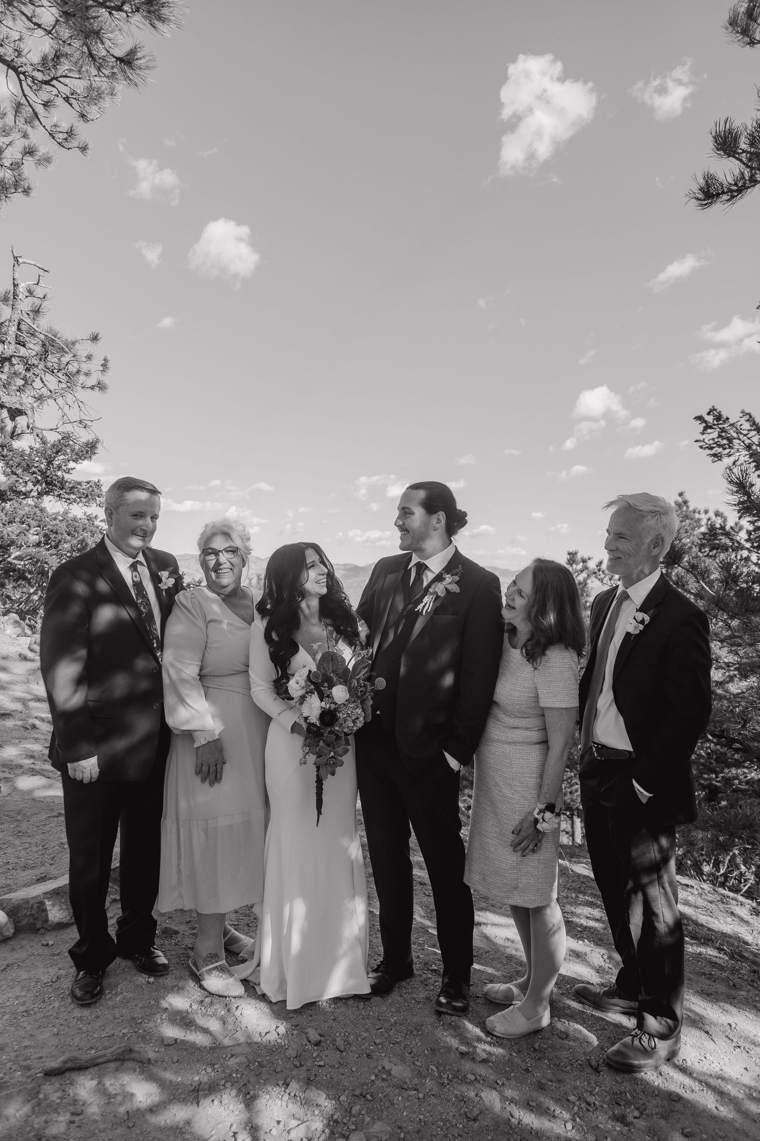 Black and white photo of bride and groom posing with family members outdoors on their wedding day.