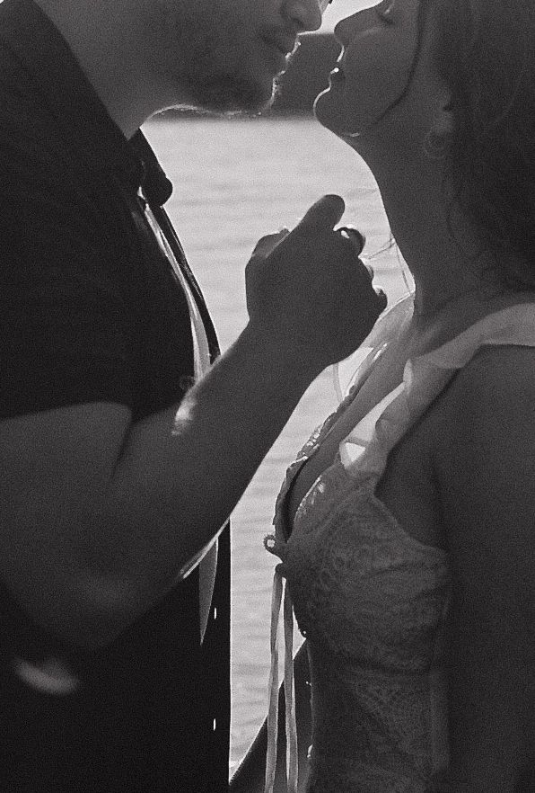 Black and white silhouette of couple holding hands and nearly kissing with water in the background.