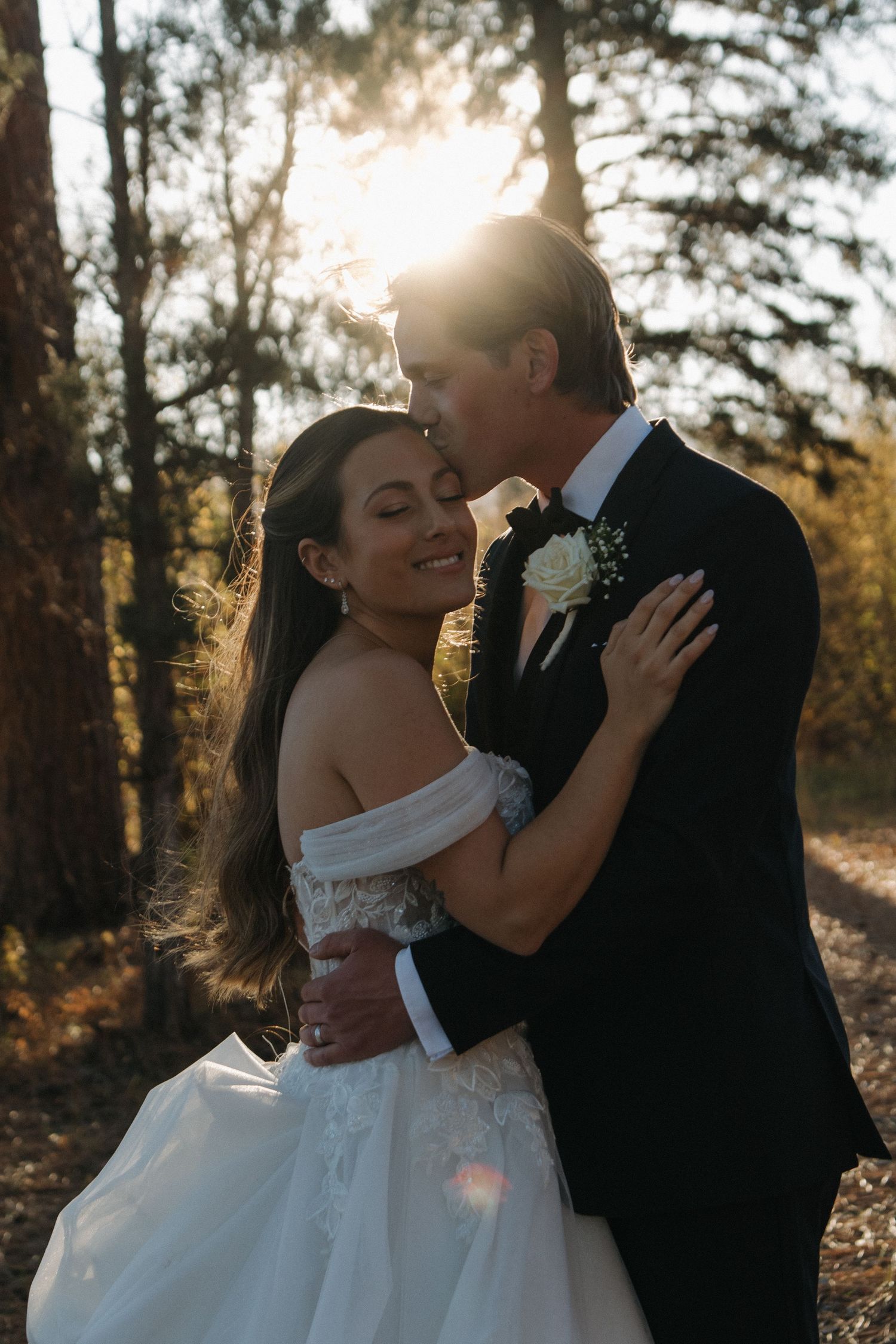 Romantic wedding couple shares intimate moments in a sunlit forest setting.