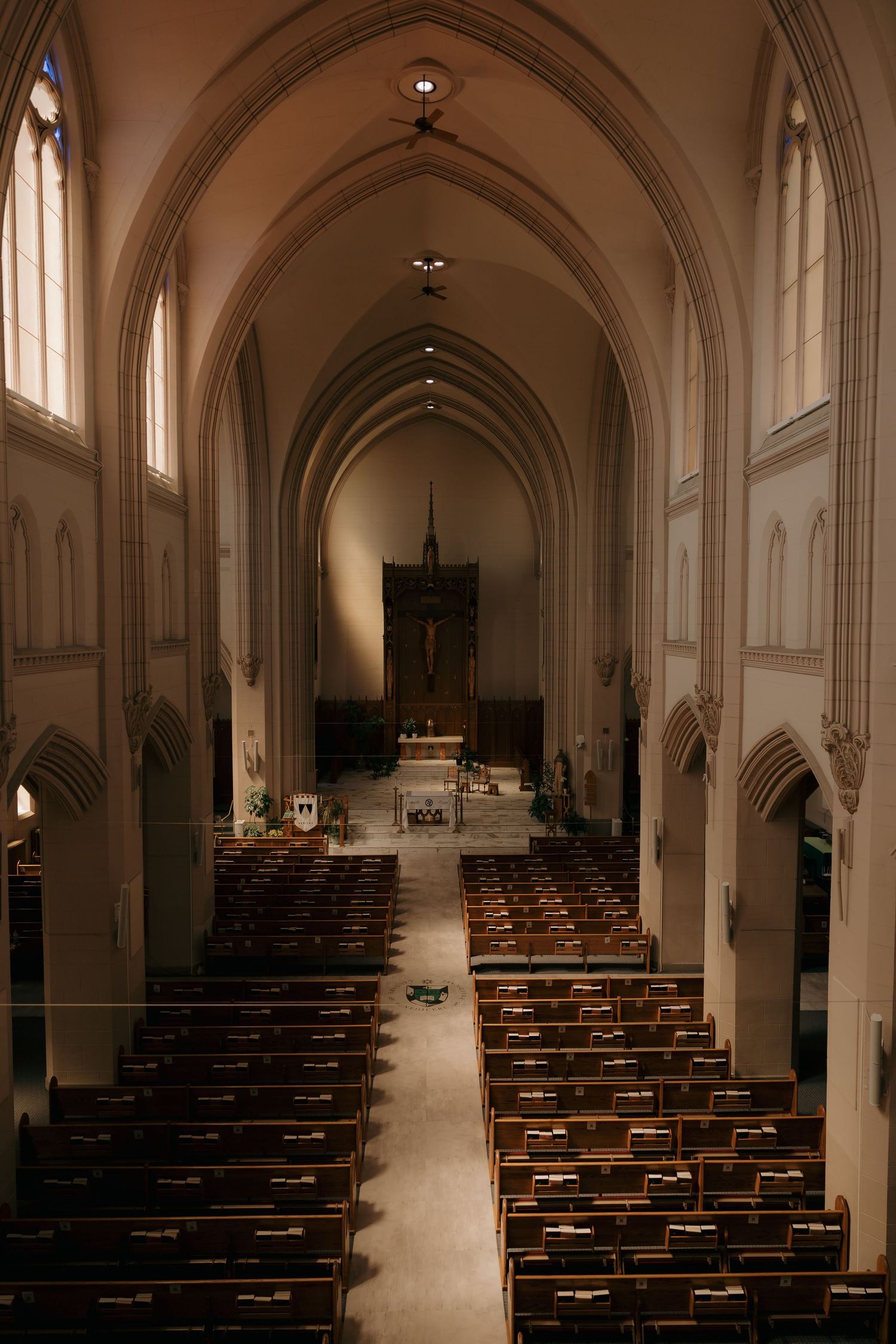 Gothic church interior with wooden pews leading to ornate altar, featuring soaring arched ceilings and tall windows.