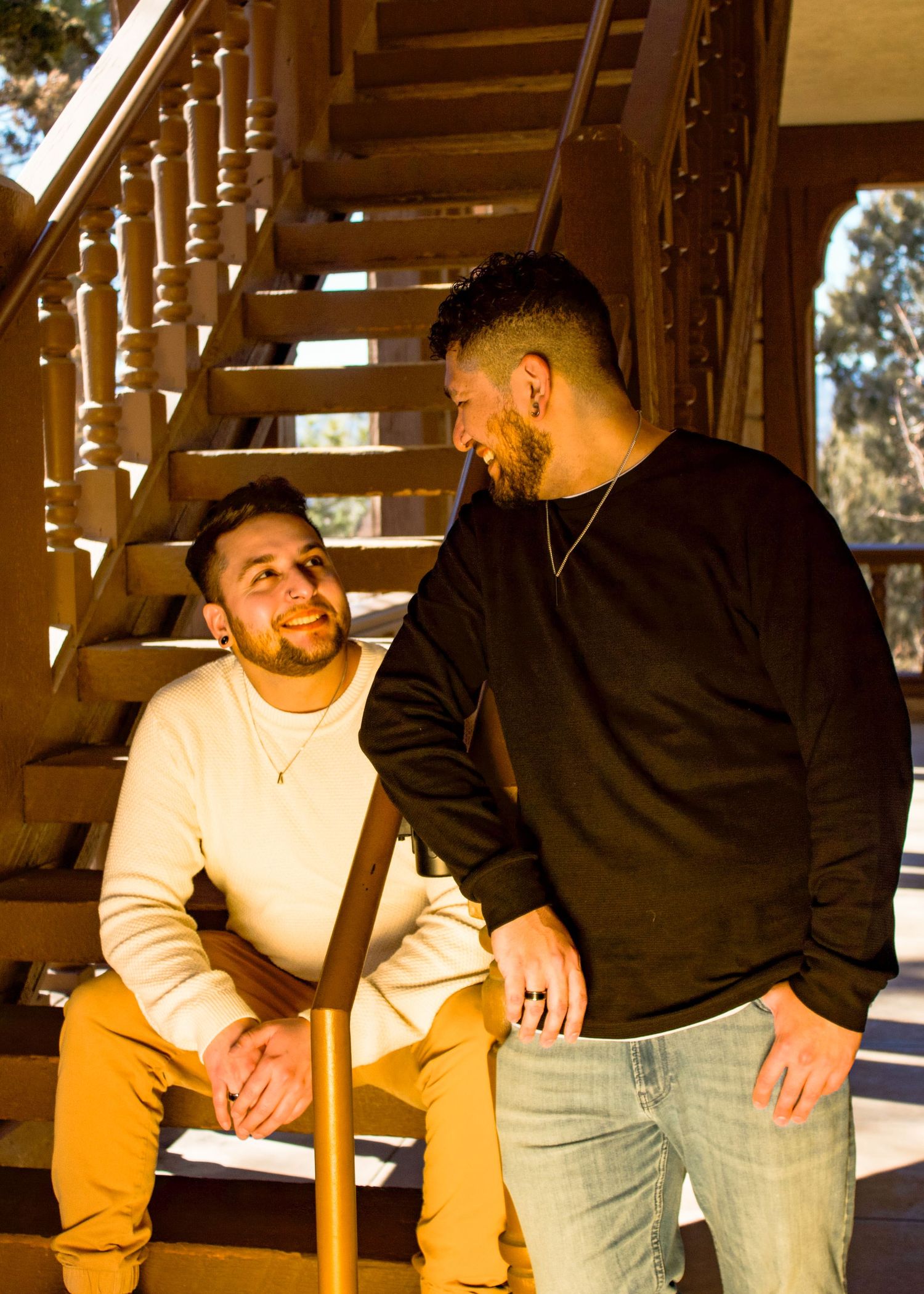 Two people share a playful moment while sitting on wooden stairs in warm sunlight.