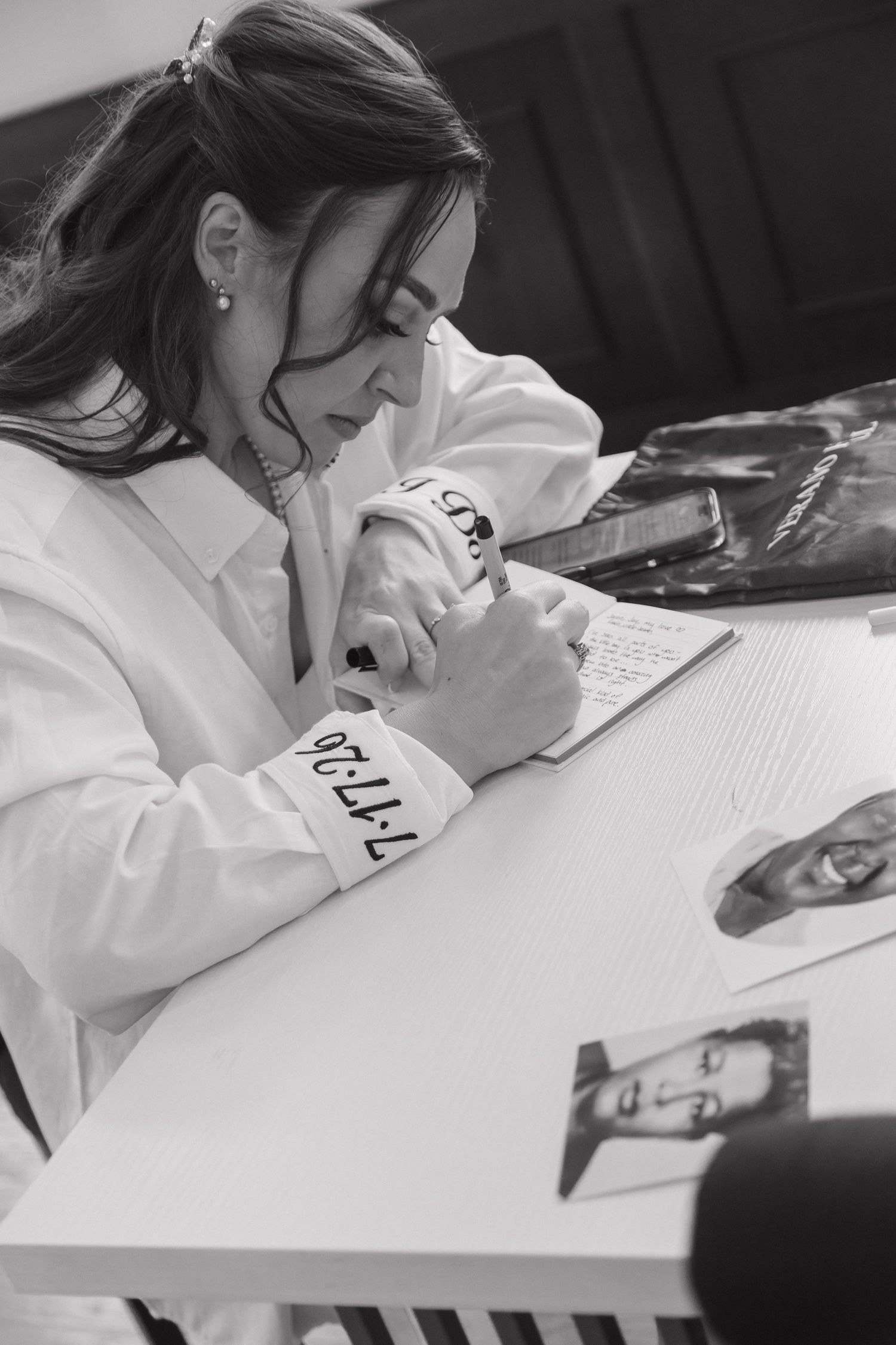 Black and white photo of a bride in a white robe signing her wedding guest book at a table.