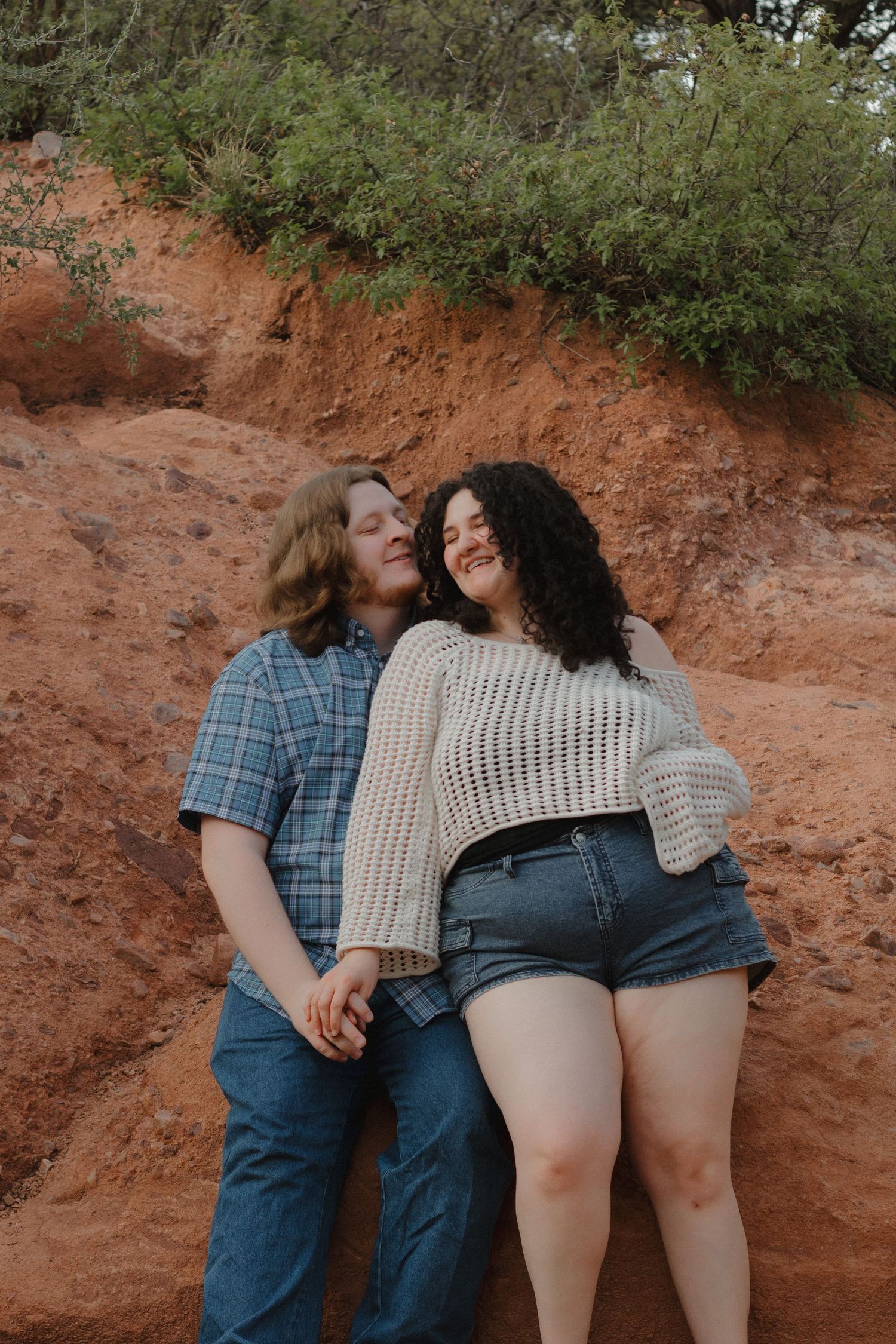Couple in denim and knit wear sitting along red rock formations in a natural setting.