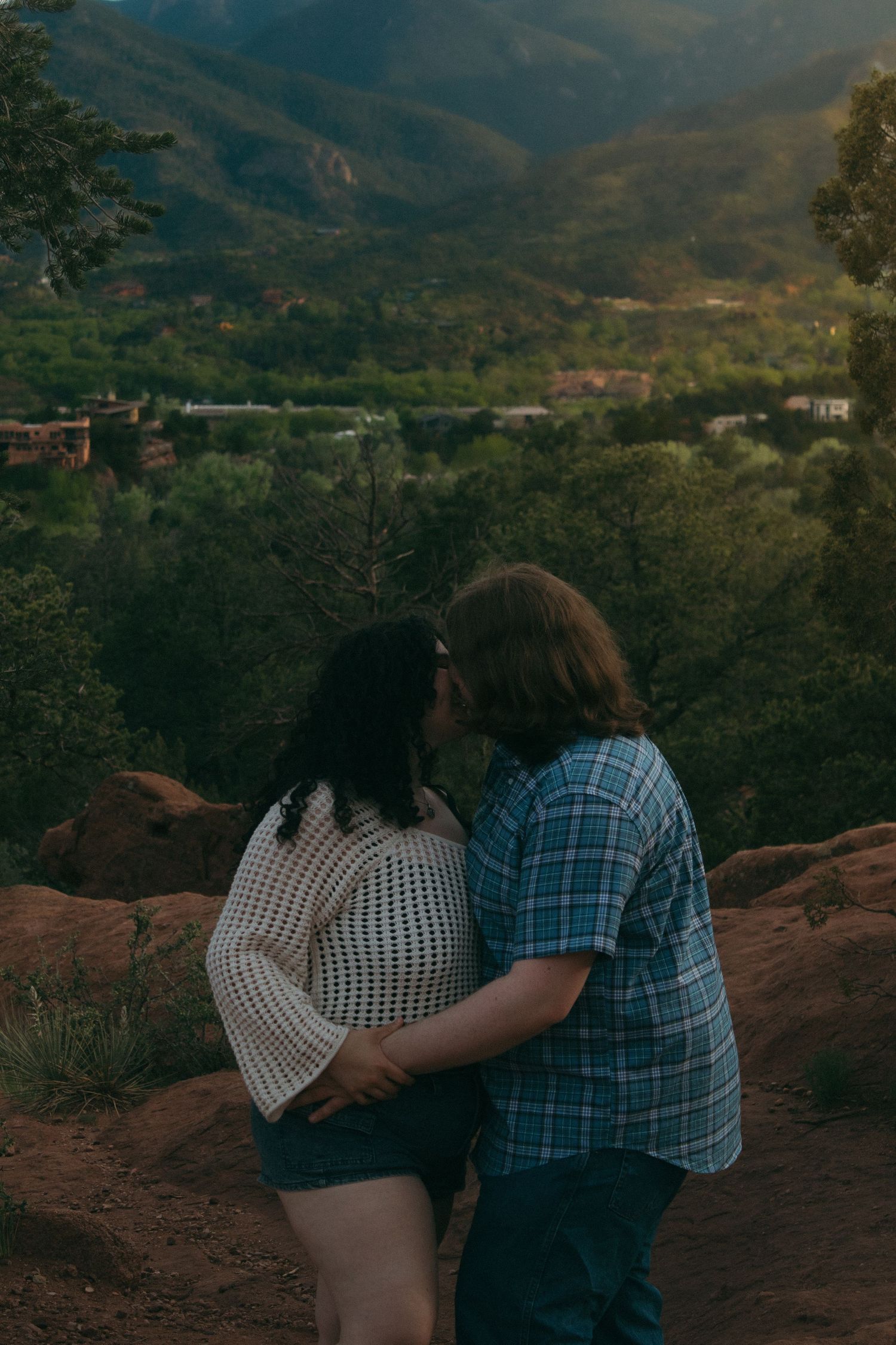 A couple shares an intimate moment while overlooking a mountain landscape at sunset.