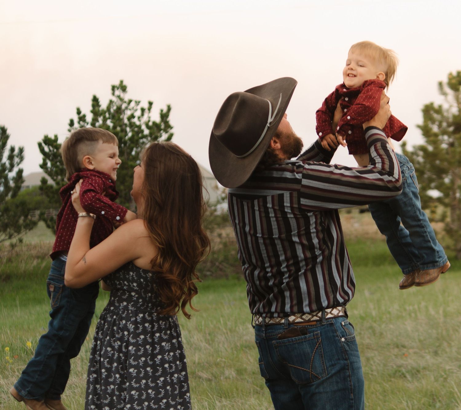 Parents lift their children playfully during a sunset photo session in a rural field.