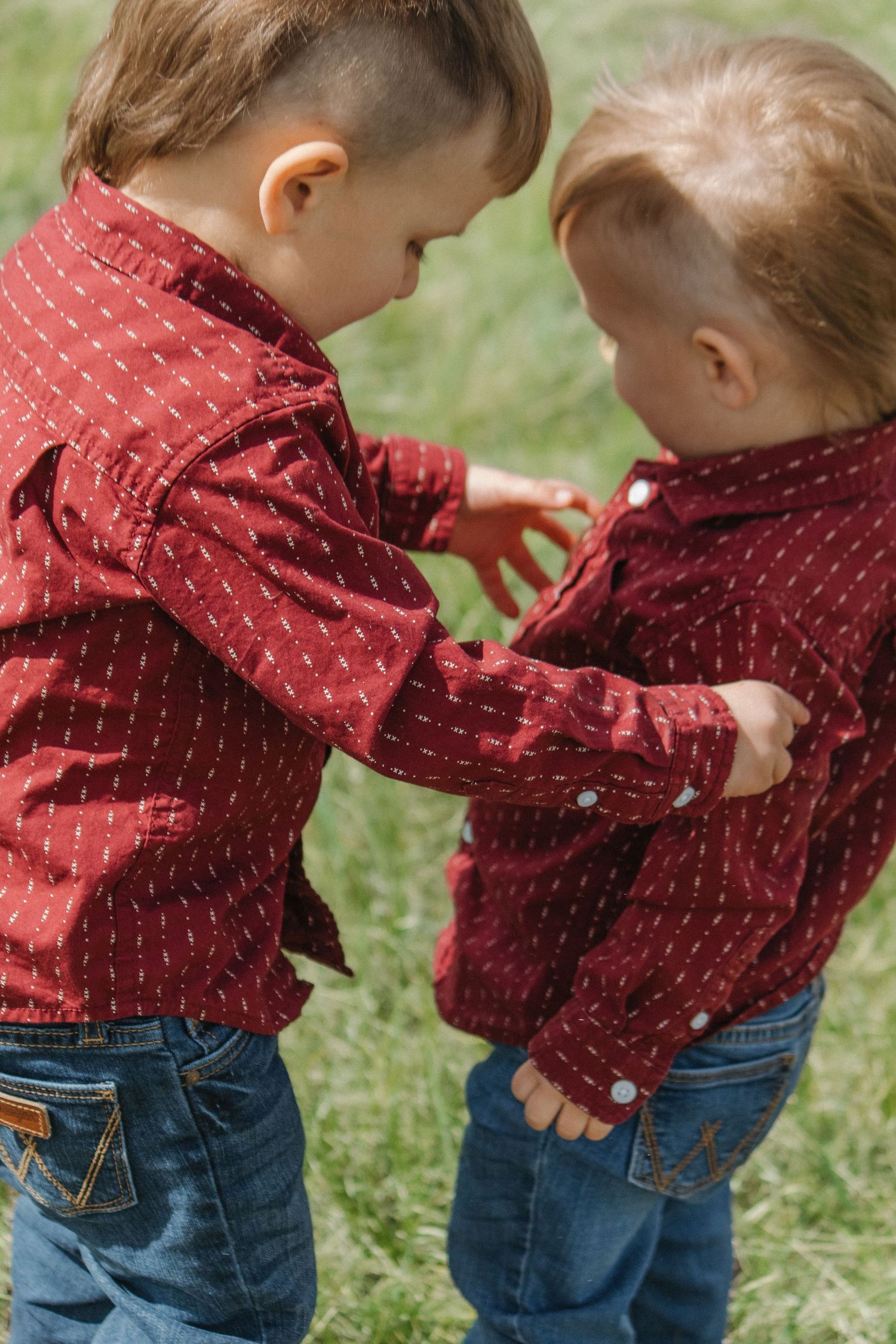Two children in matching red shirts and jeans playing together outdoors.