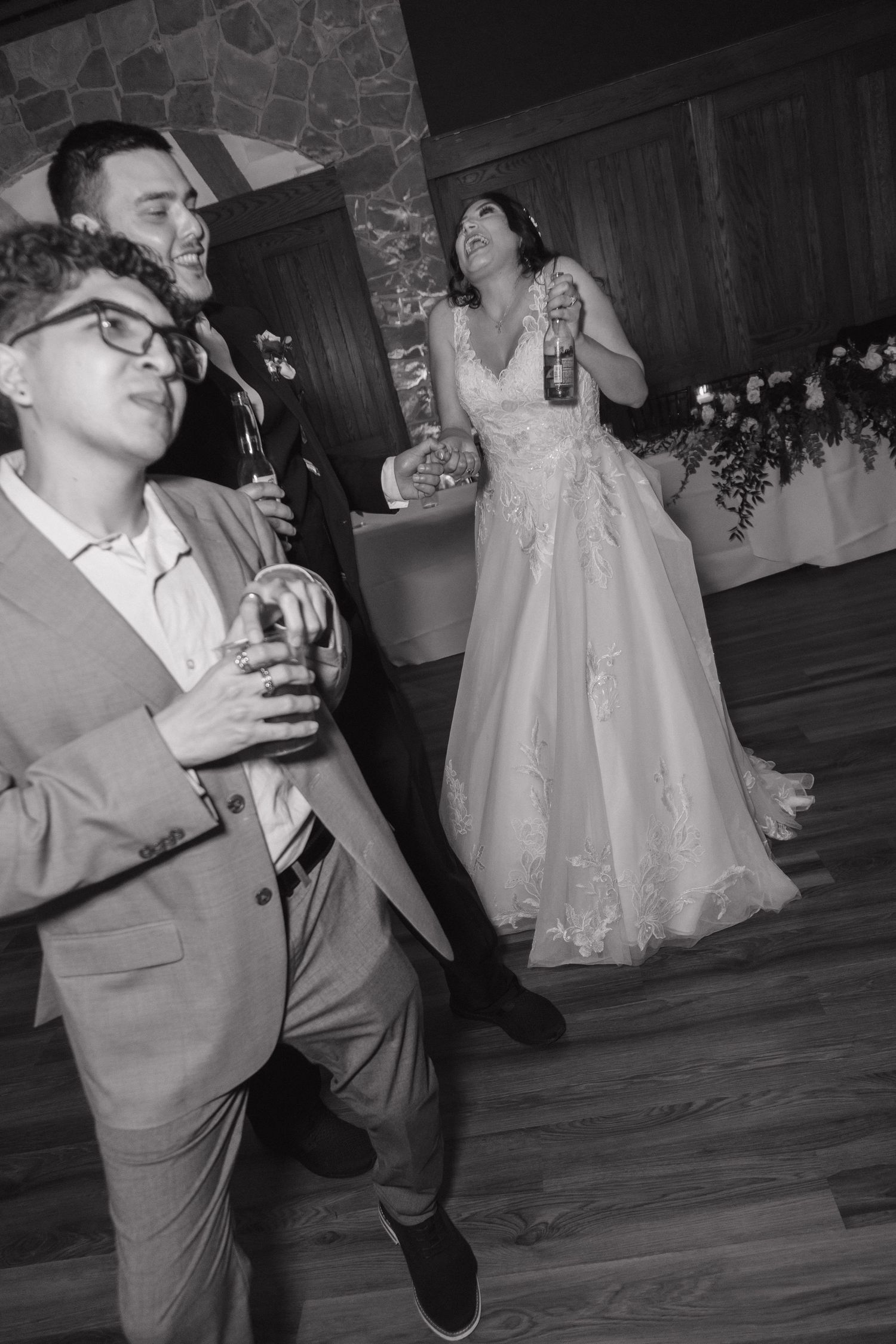 Black and white photo of bride and guests dancing joyfully at wedding reception.