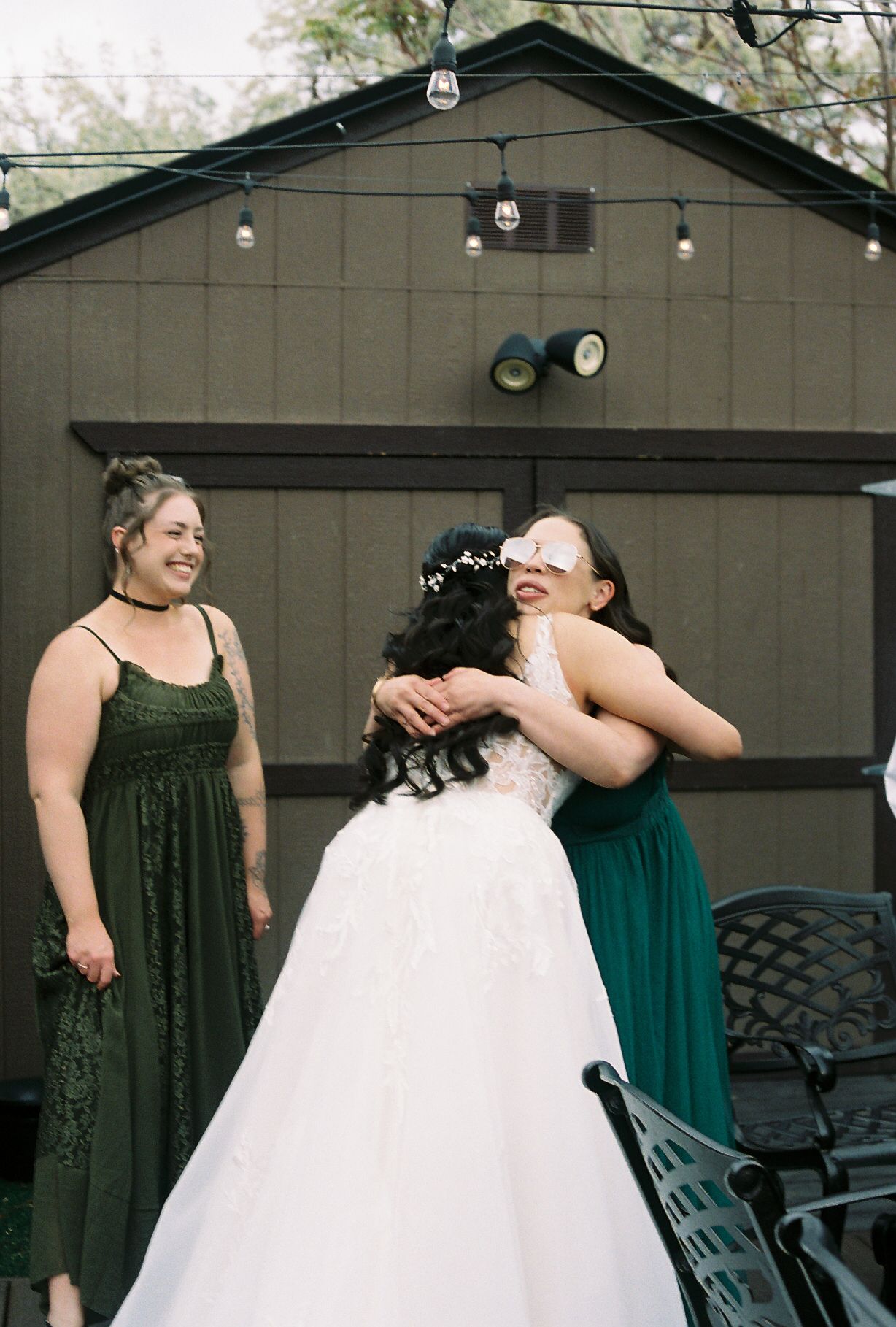 Bride hugging a guest wearing novelty glasses while bridesmaid looks on at wedding.