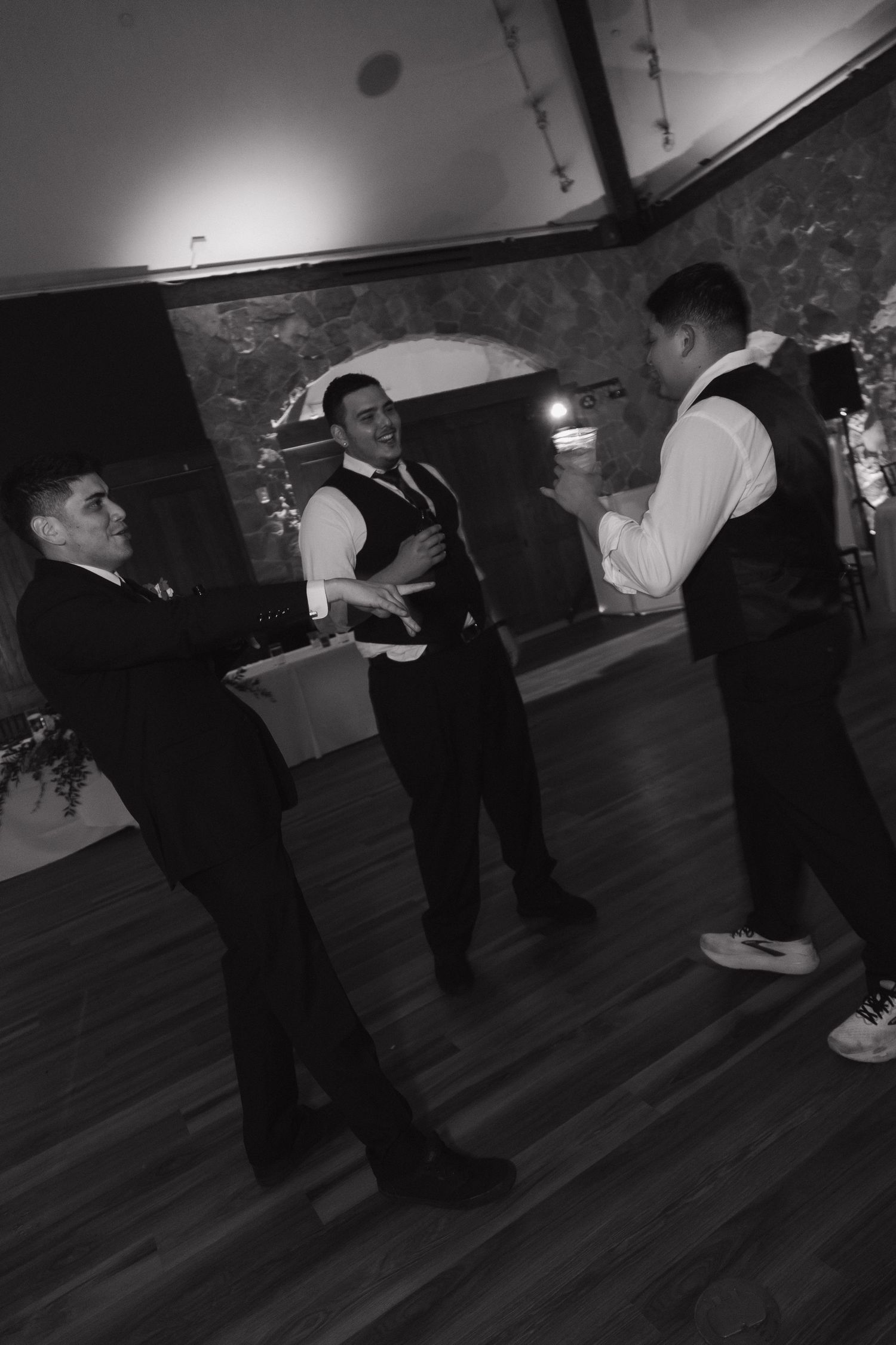 Black and white photo of three groomsmen socializing on the dance floor at wedding reception.