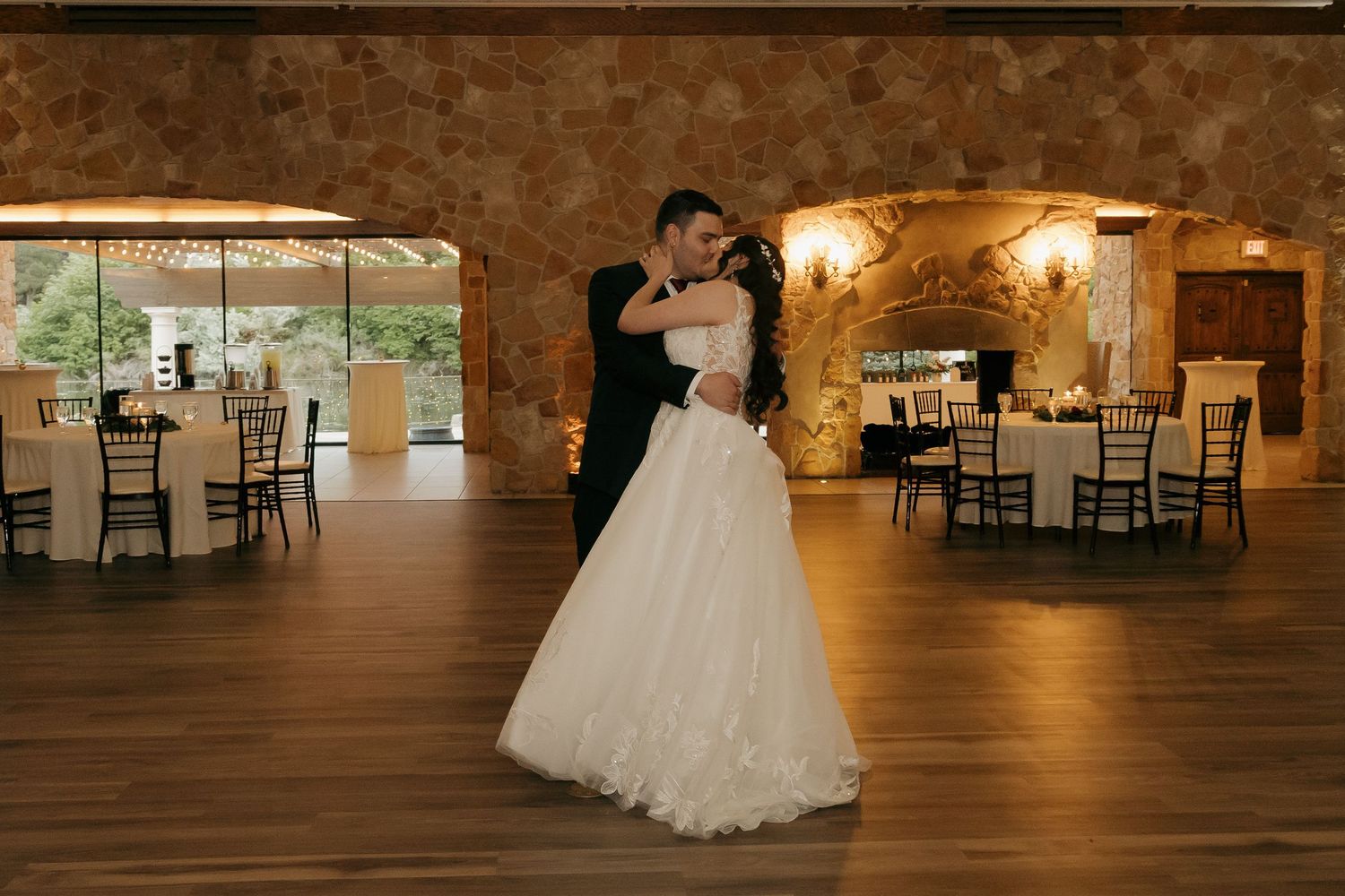 Bride and groom share a romantic embrace during their first dance in a rustic stone wedding venue.