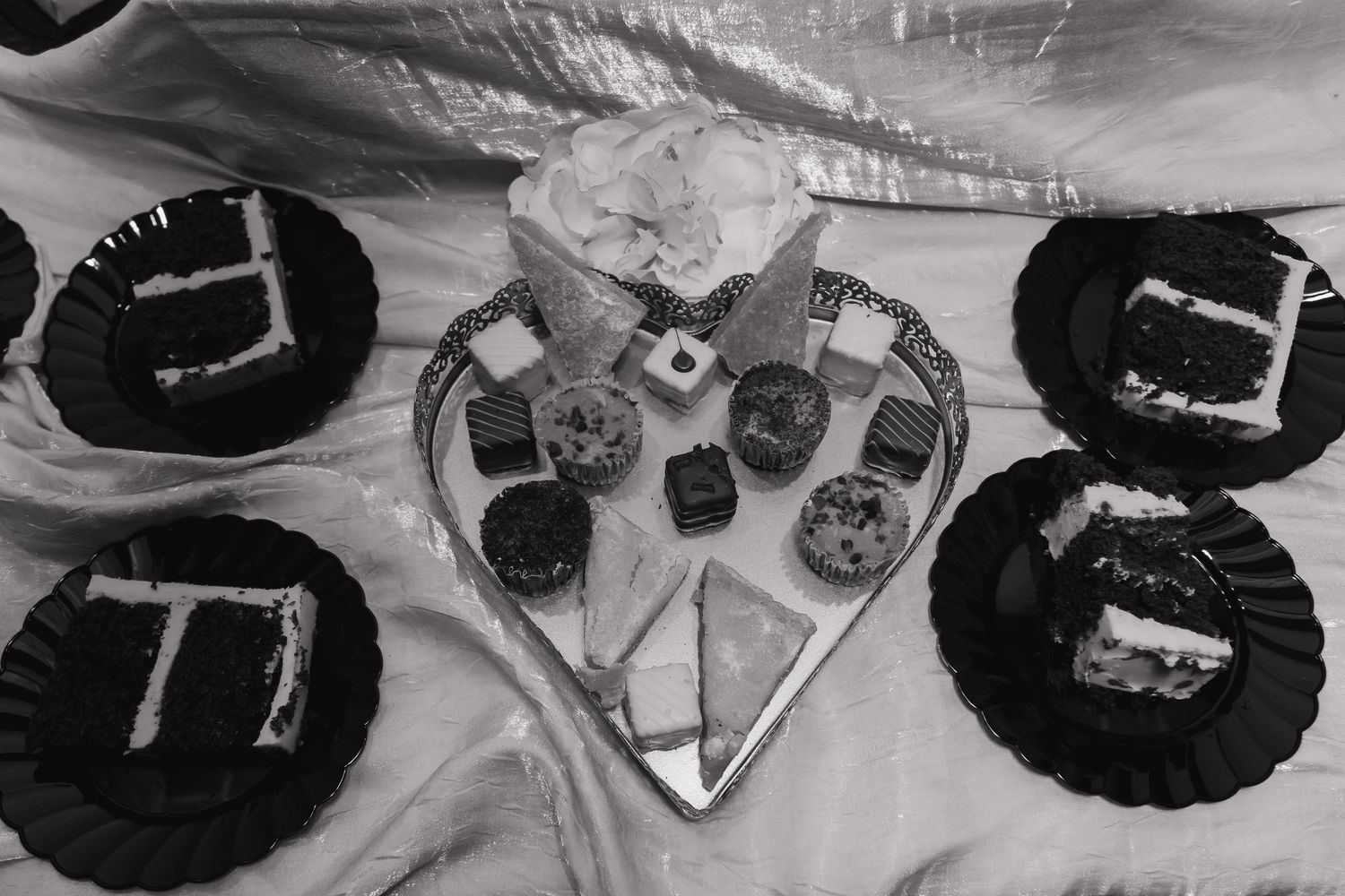 Wedding dessert table with decorated cupcakes and small cake on heart-shaped platter in black and white.