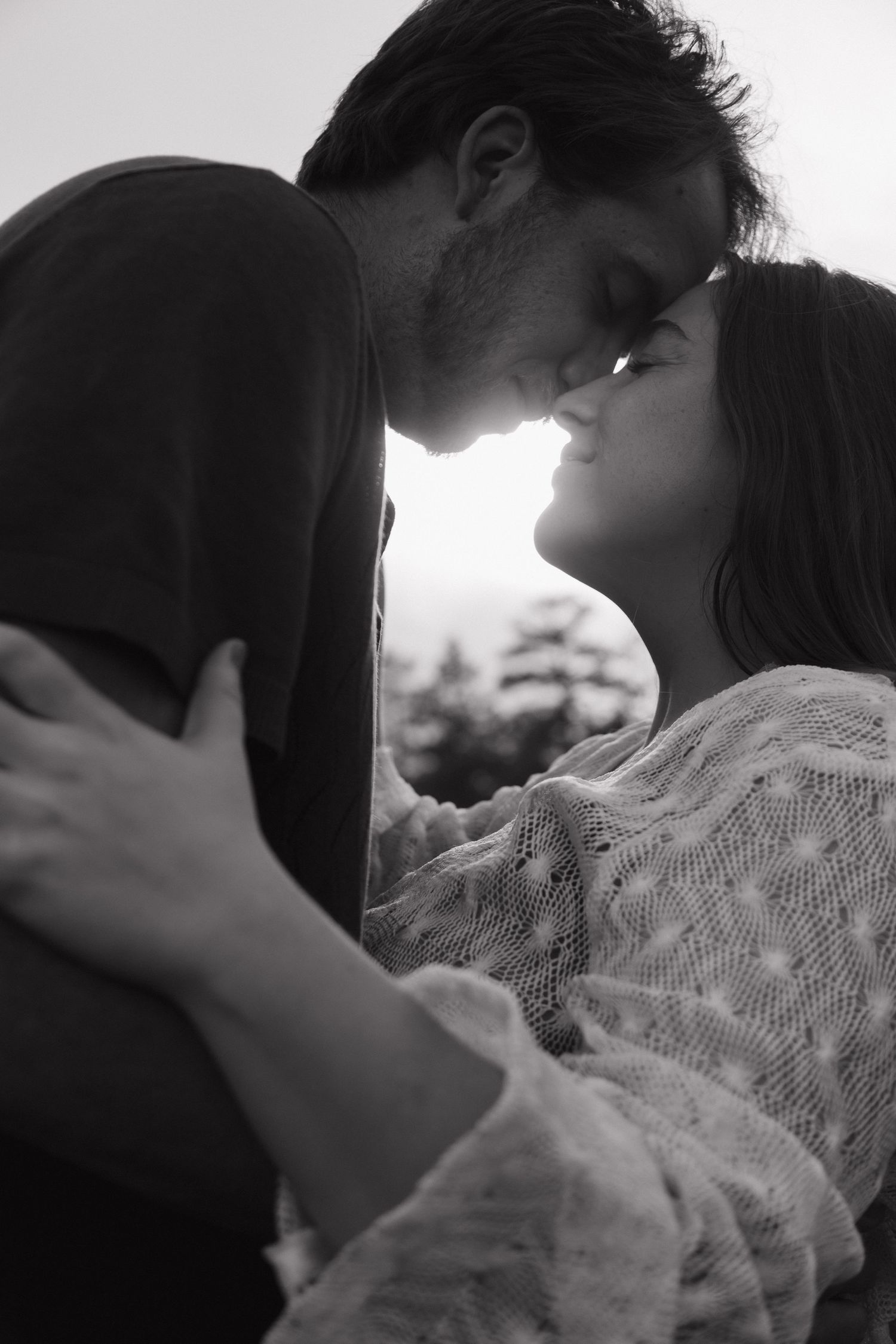 Black and white photo of a romantic couple about to kiss outdoors.