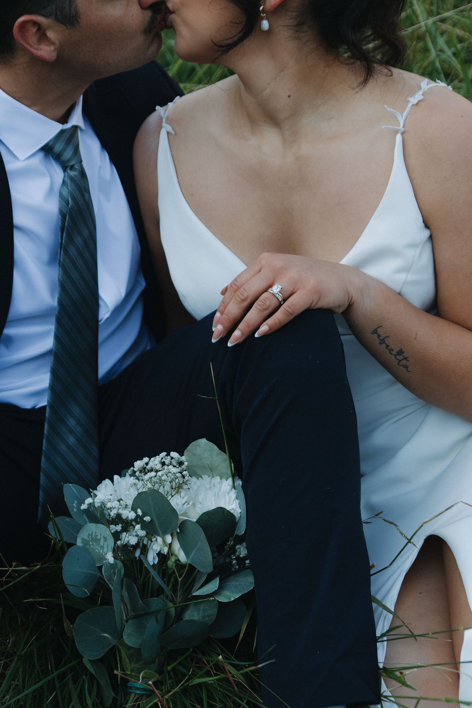 A romantic wedding photo showing a close-up view of a couple embracing outdoors with greenery in the background.