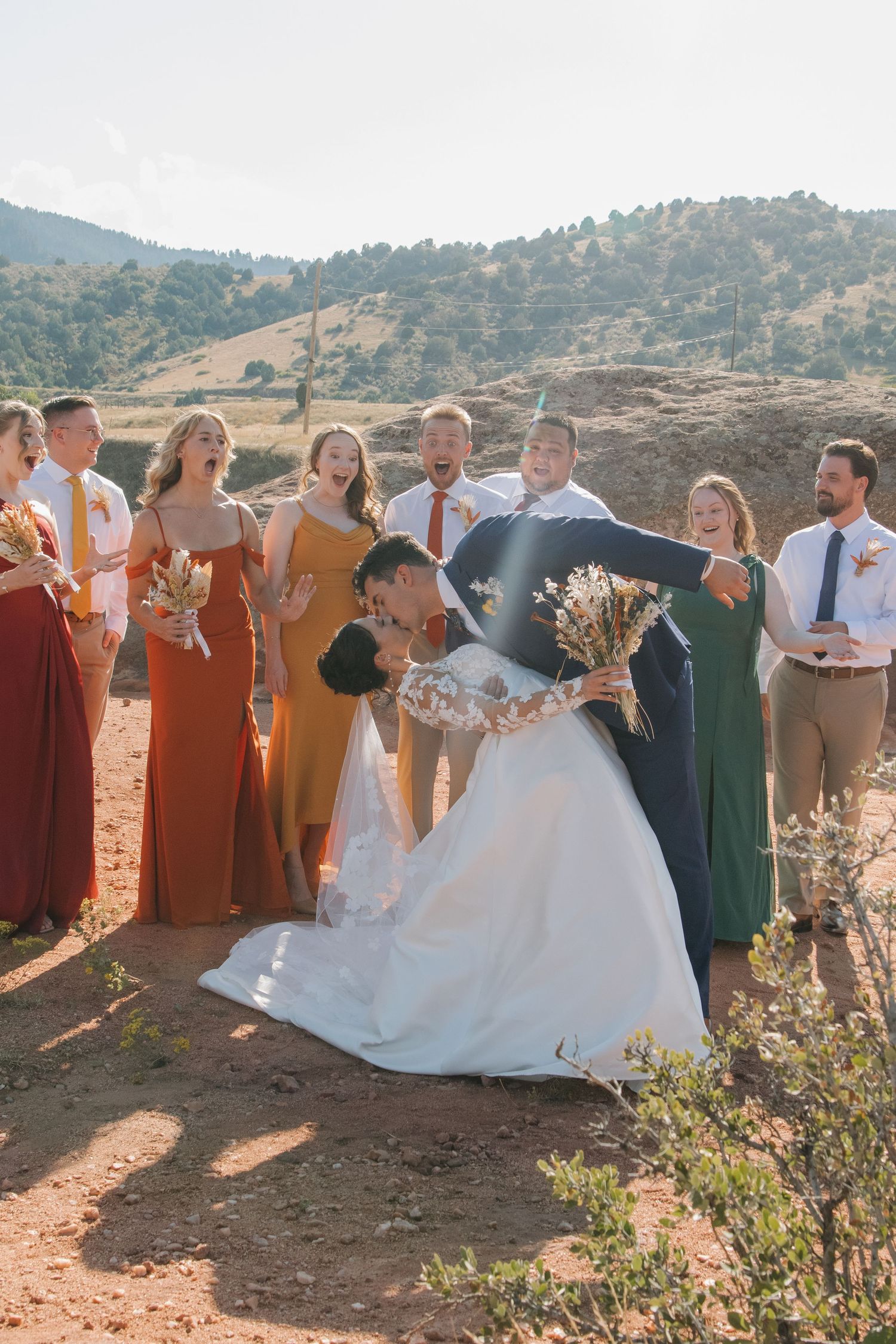 Wedding party celebrates joyfully against scenic mountain backdrop in outdoor setting.