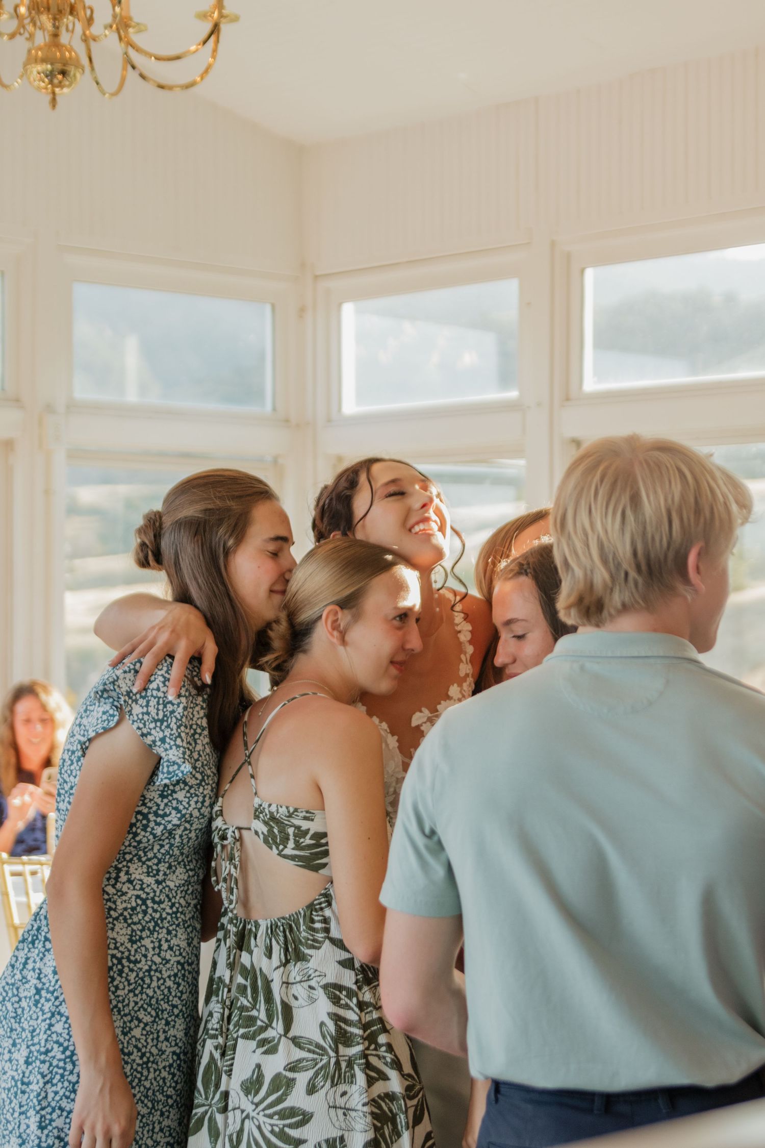 Group of wedding party members sharing an emotional group hug in a sunlit room.