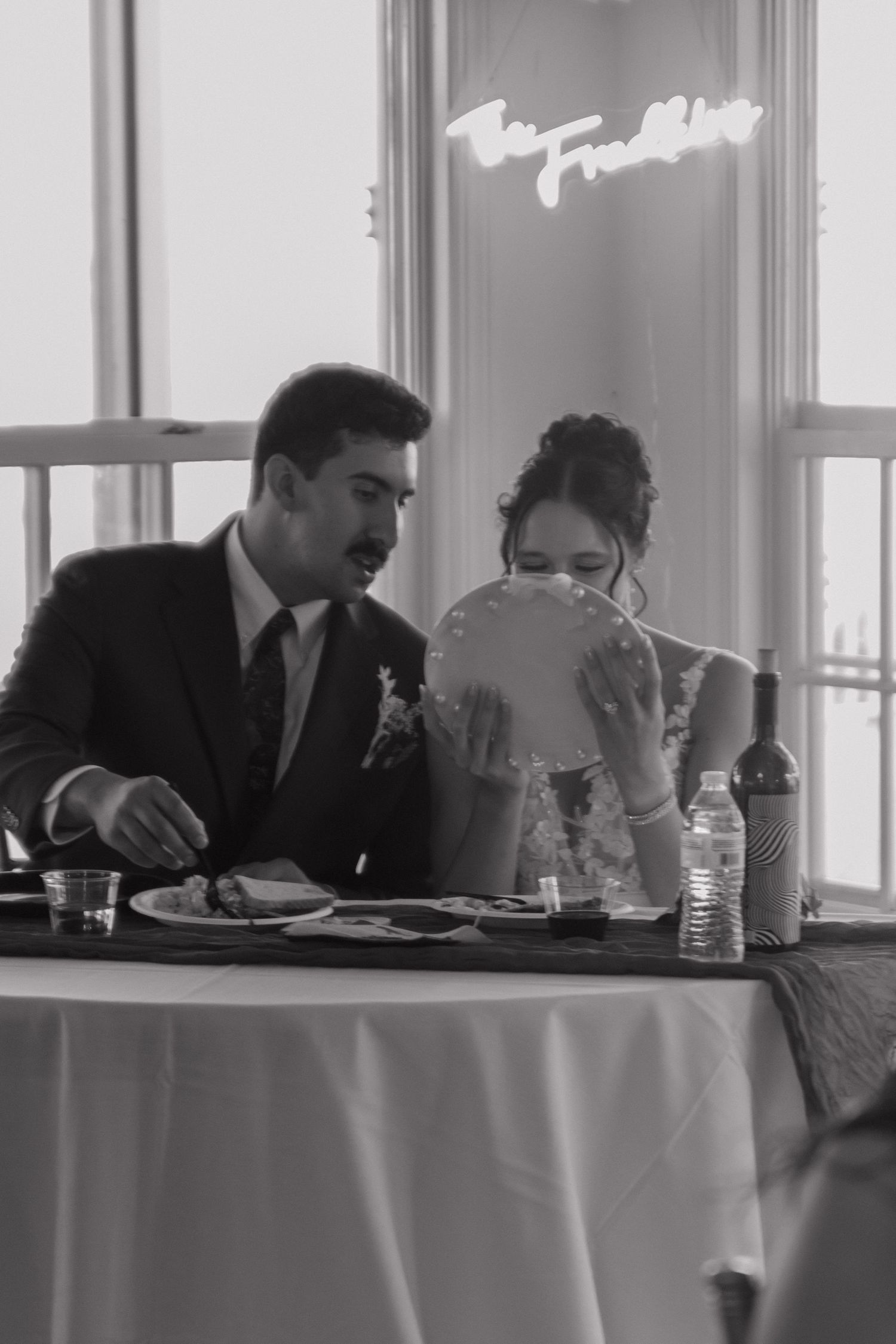 Wedding reception head table with guests sharing candid moments in black and white.