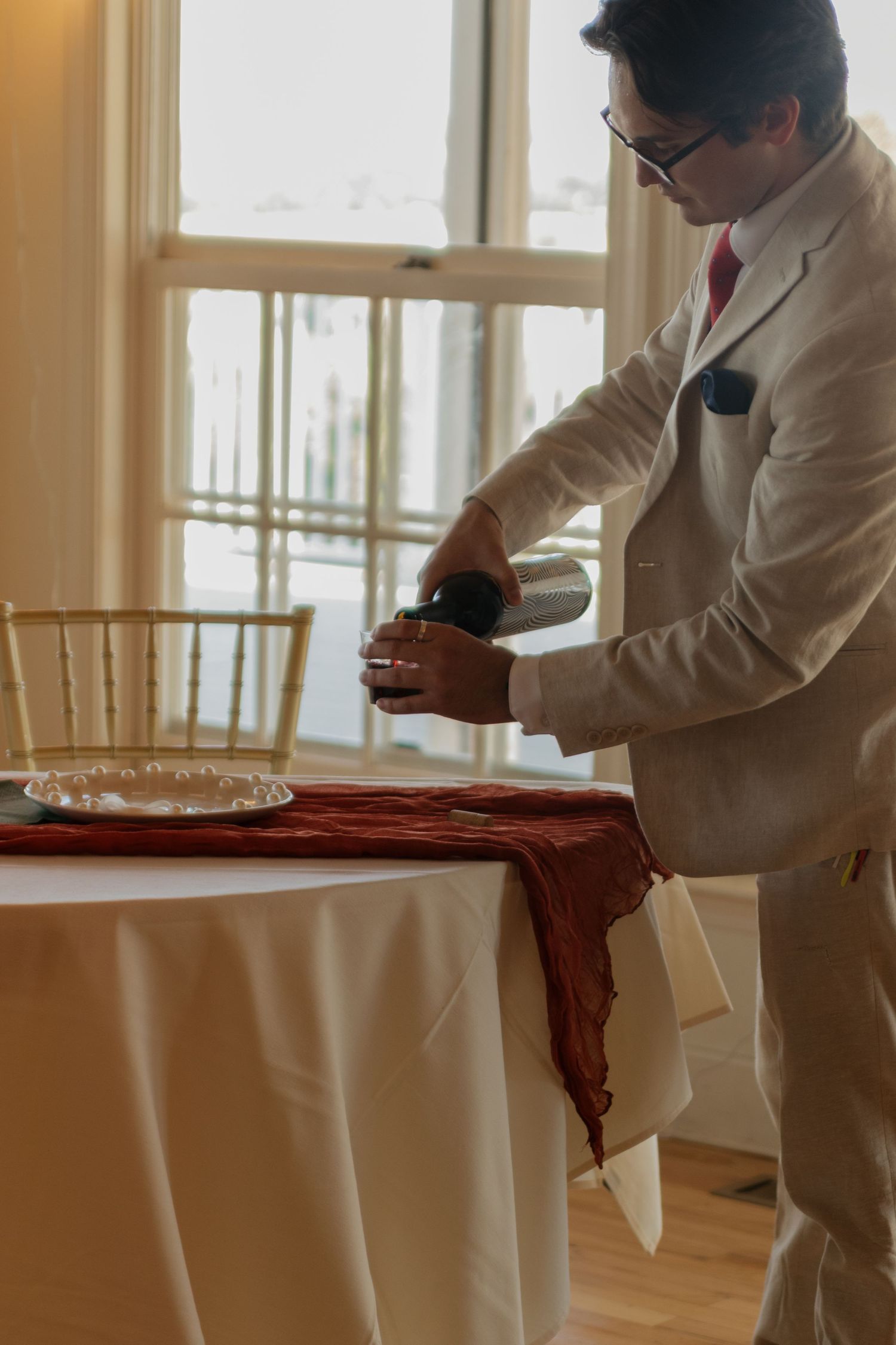 Person in white suit adjusting tablecloth at wedding reception setup.