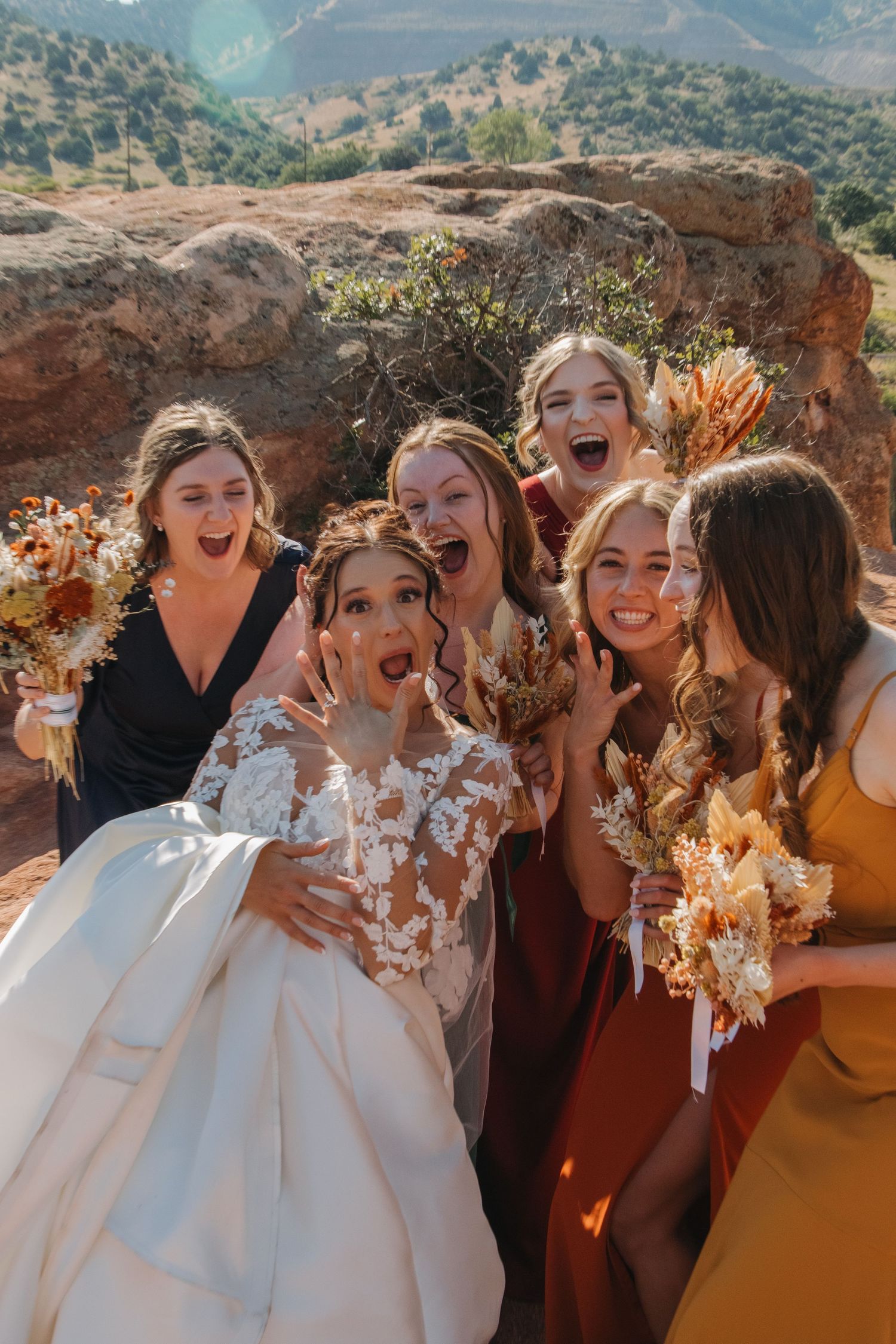 Wedding party laughs together against scenic mountain backdrop in warm sunlight.