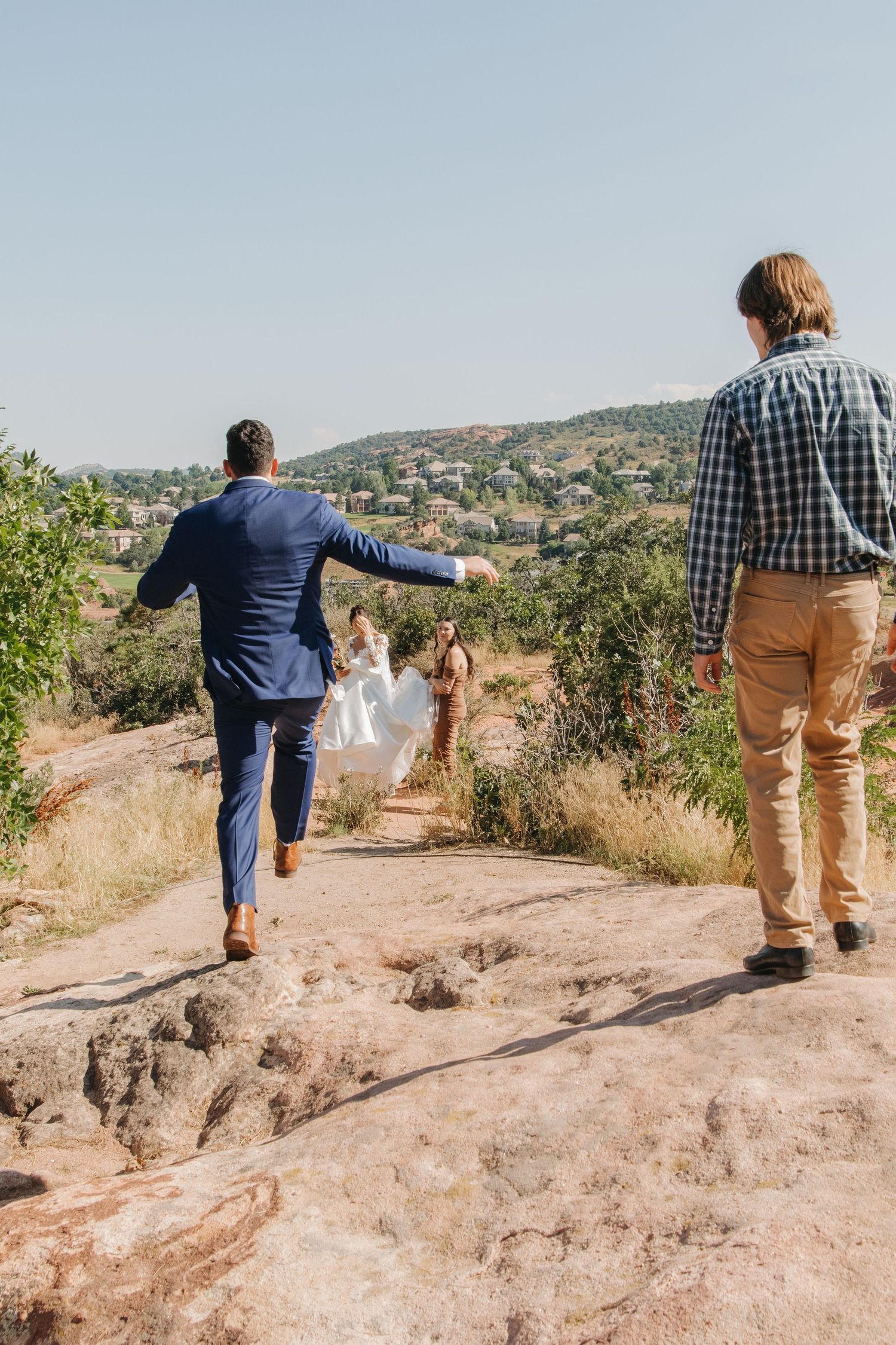Two figures walk along a rocky desert trail into scenic mountainous landscape.