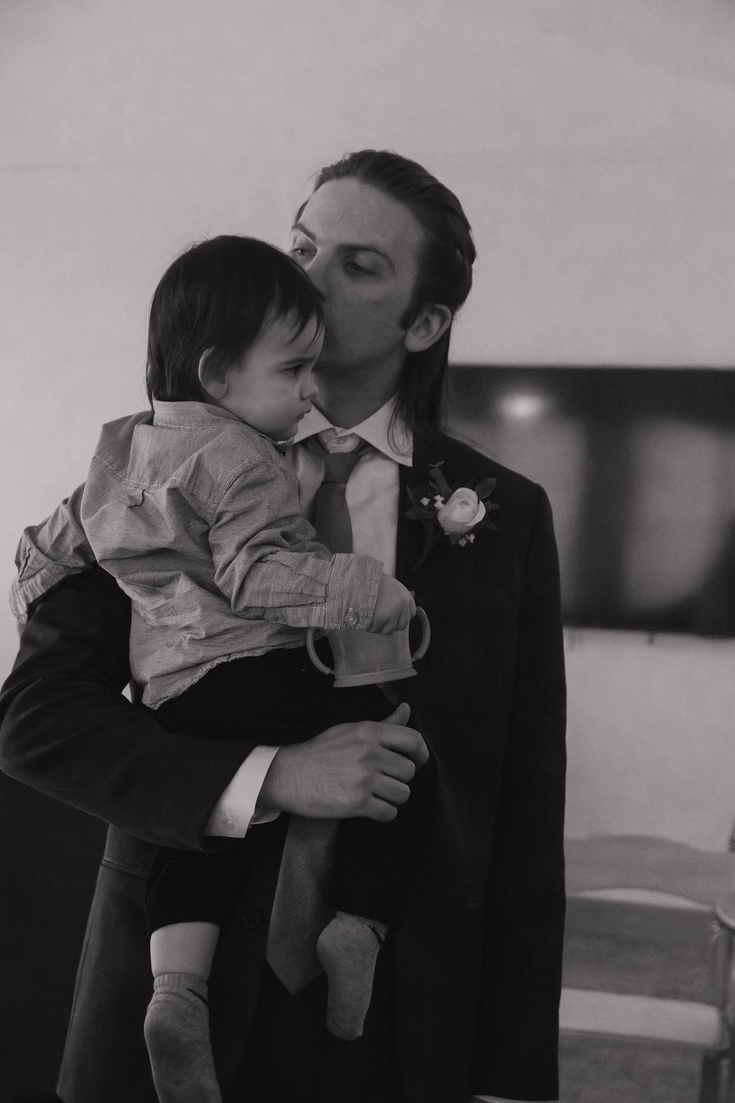 A tender black and white moment between a suited figure and small child at a formal event.