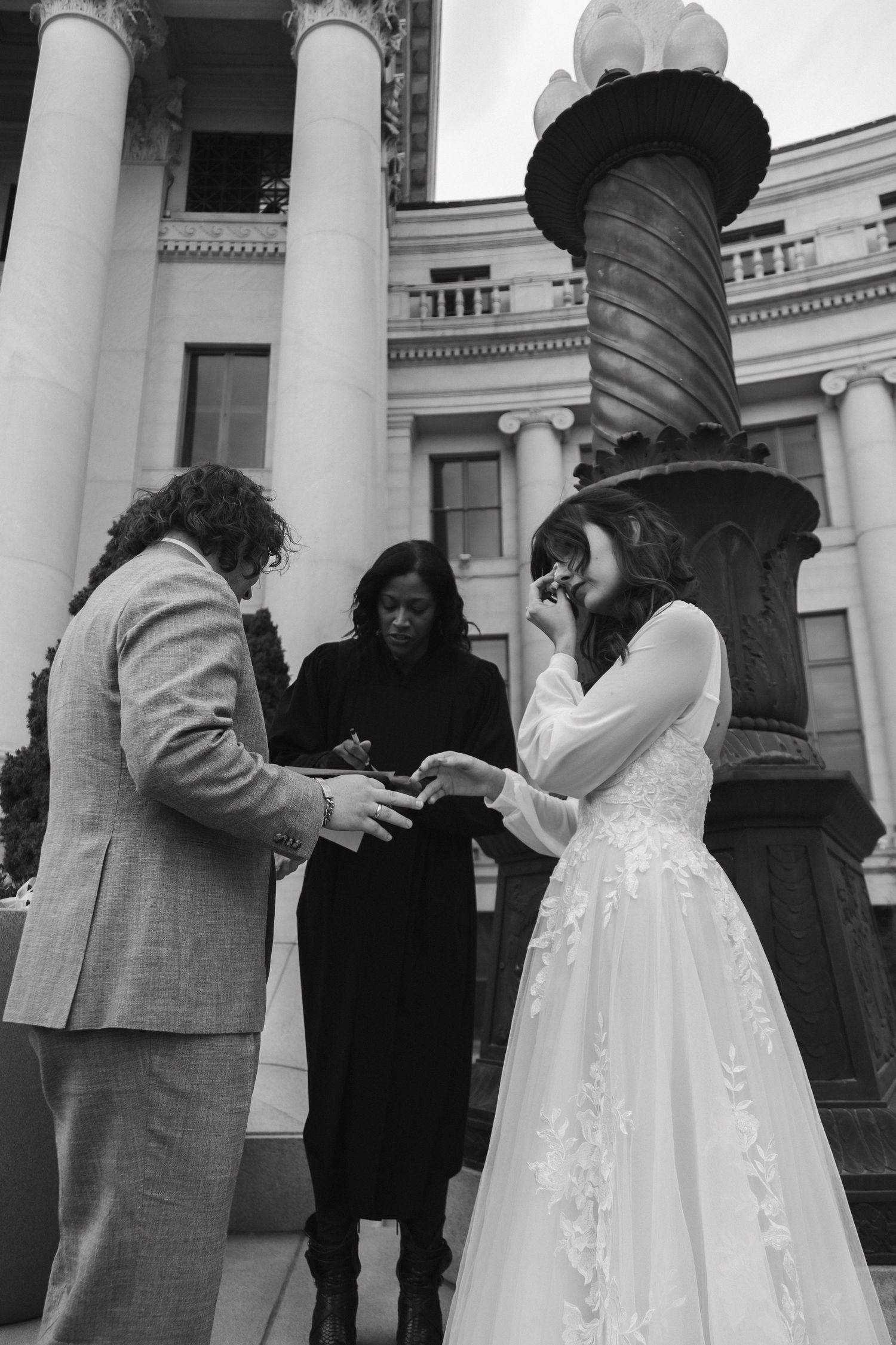 A wedding ceremony takes place on marble steps with elegant white columns in the background.