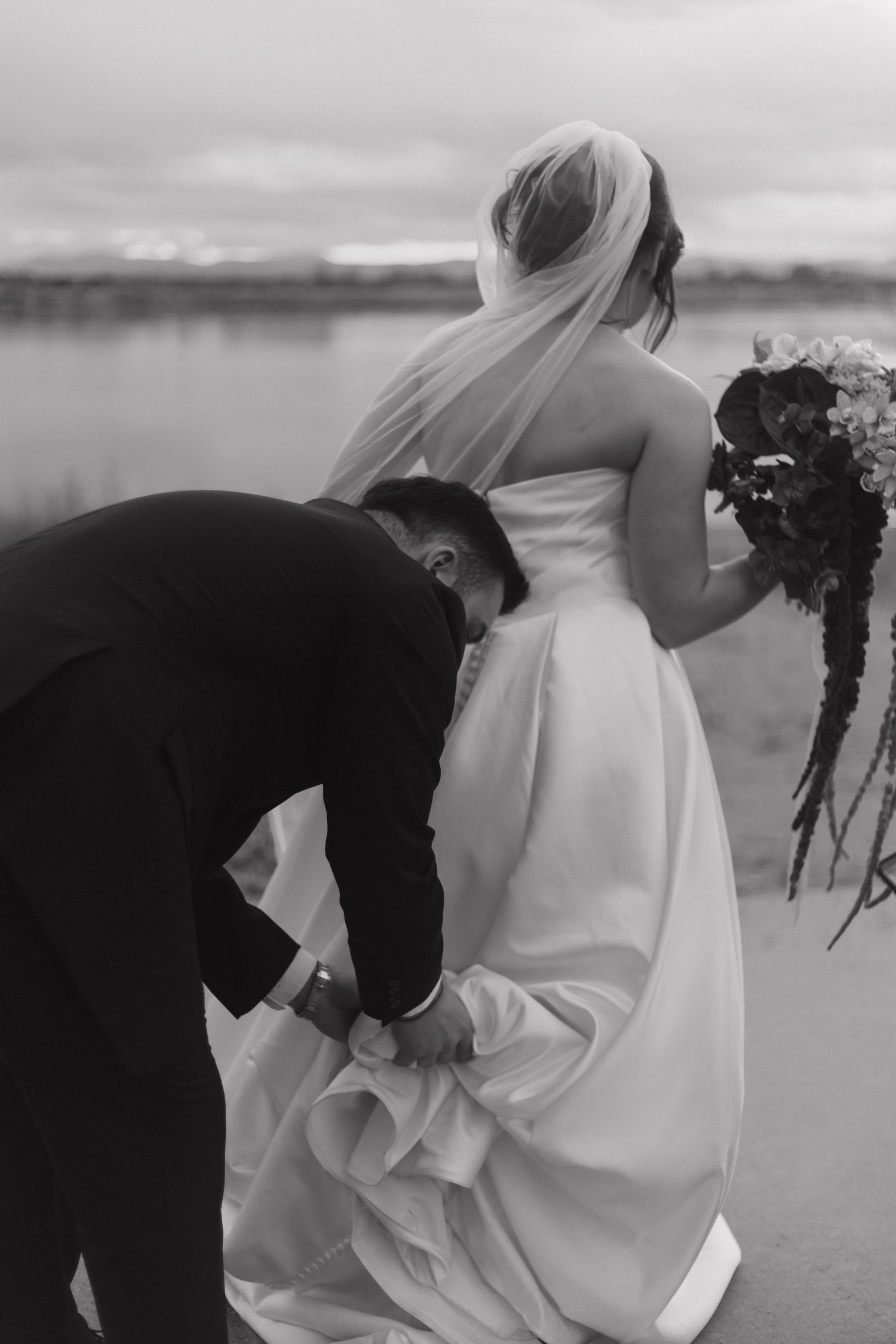 A couple in formal attire shares a moment on a windy beach.