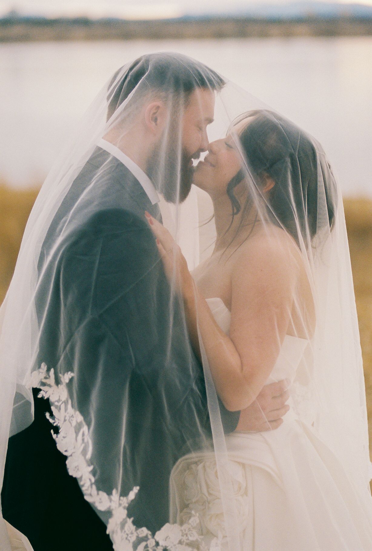 A dreamy wedding portrait shows a couple sharing an intimate moment through a delicate veil.