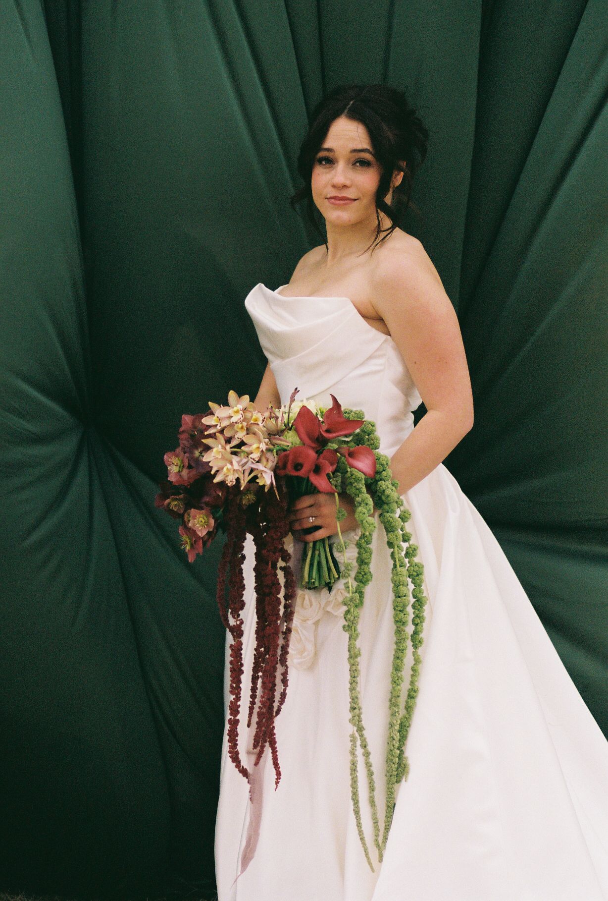 A bride in a white gown holds a cascading bouquet with burgundy and green florals.