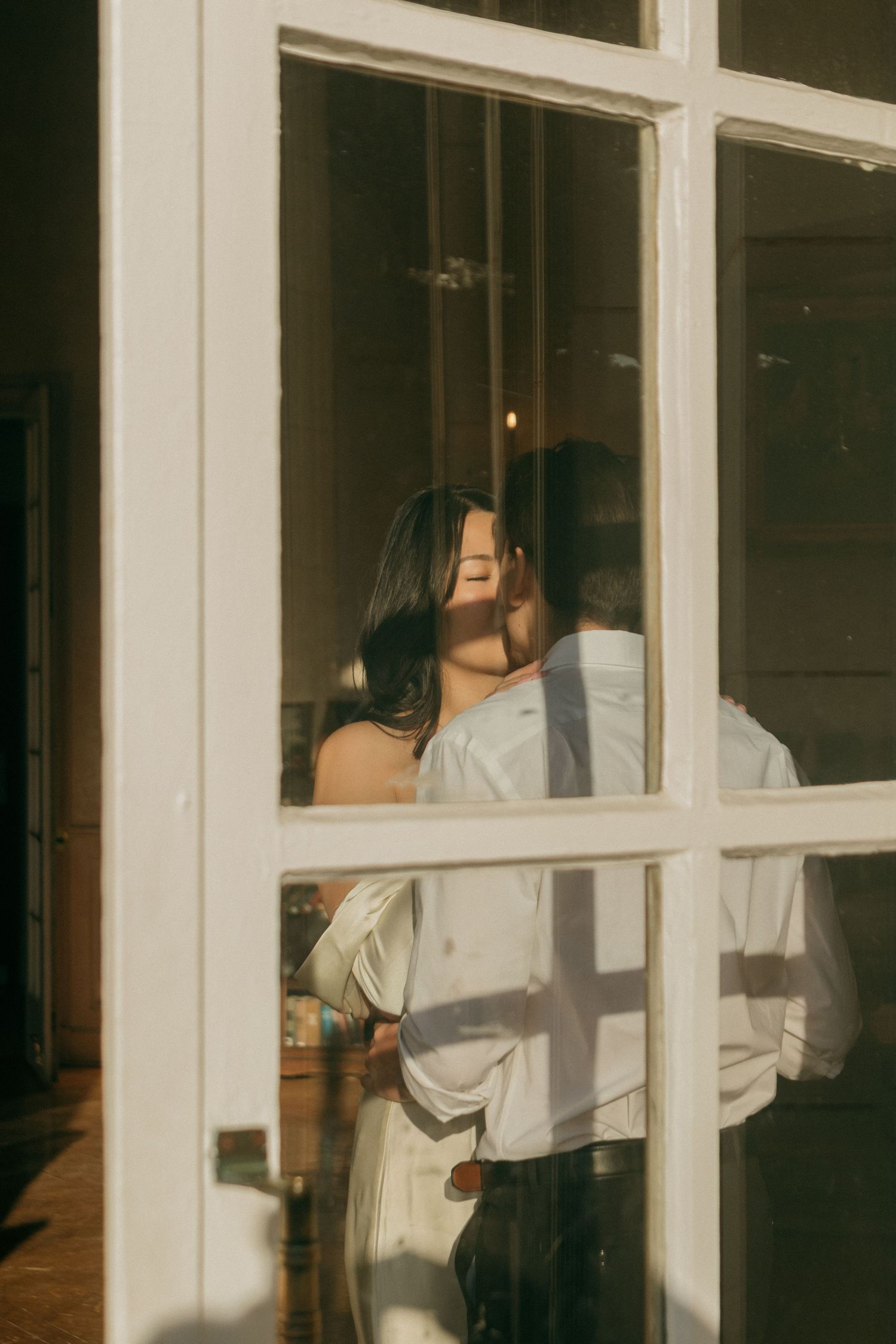 A couple's silhouette is visible through white window panes in a romantic scene.