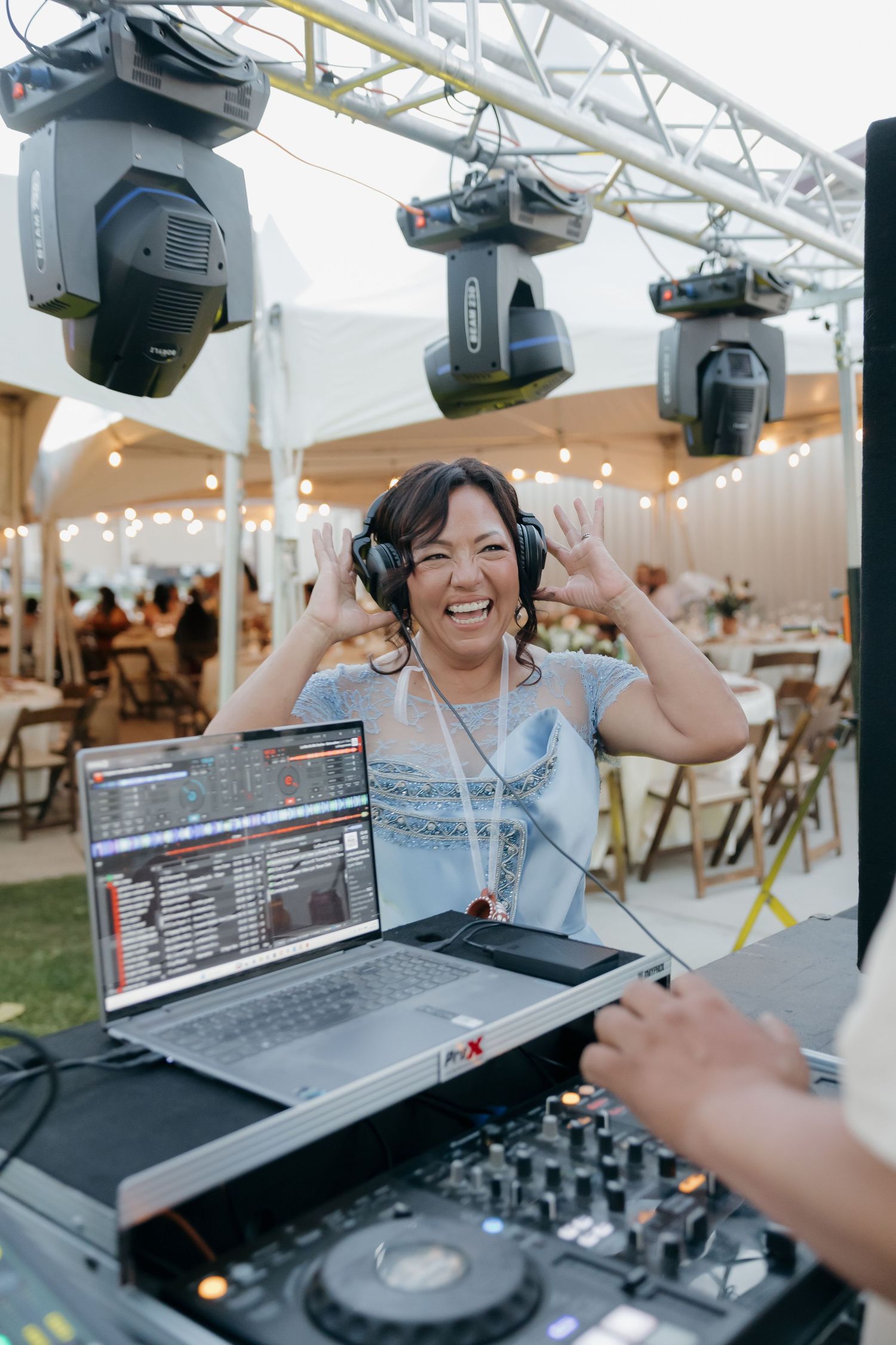 Smiling female DJ with headphones performs at outdoor wedding reception under tent.
