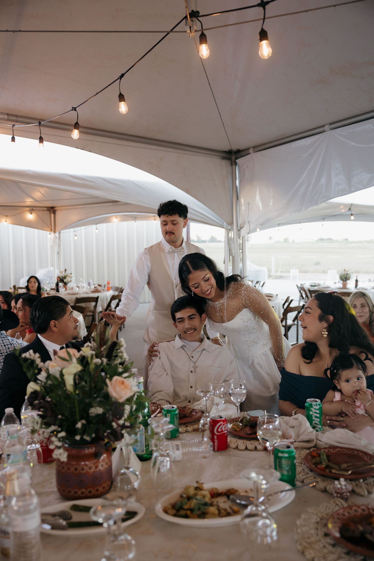 A bride and groom share a joyful moment with family at a decorated wedding reception dinner table.