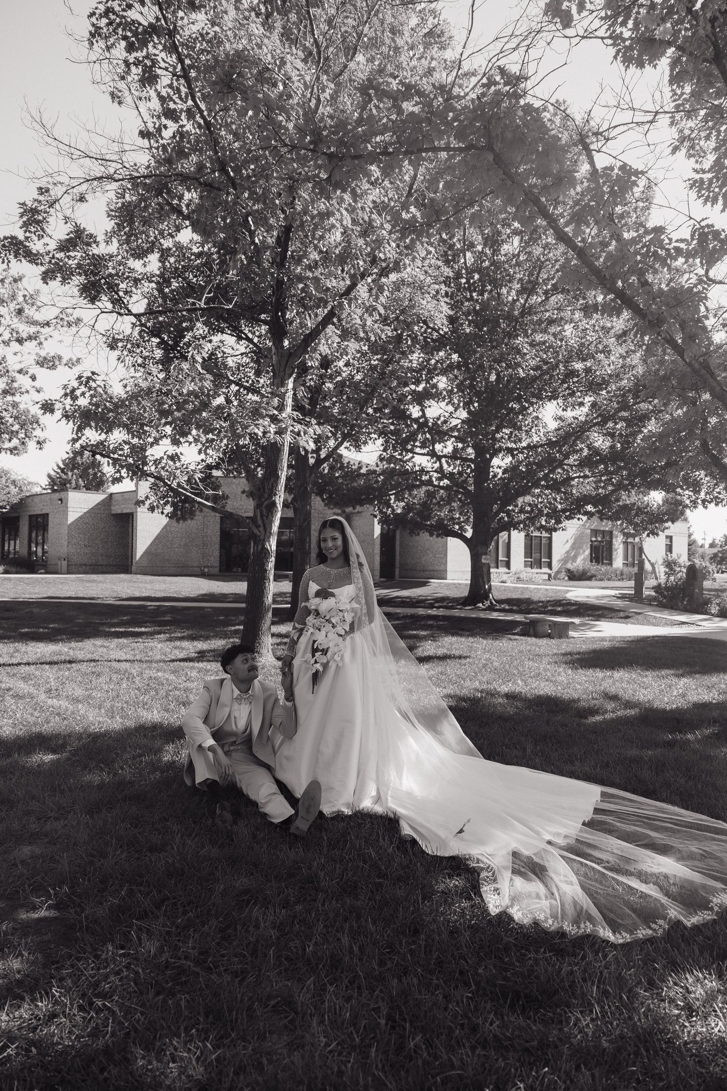 A bride and groom pose under a large tree in a stunning black and white outdoor wedding portrait.
