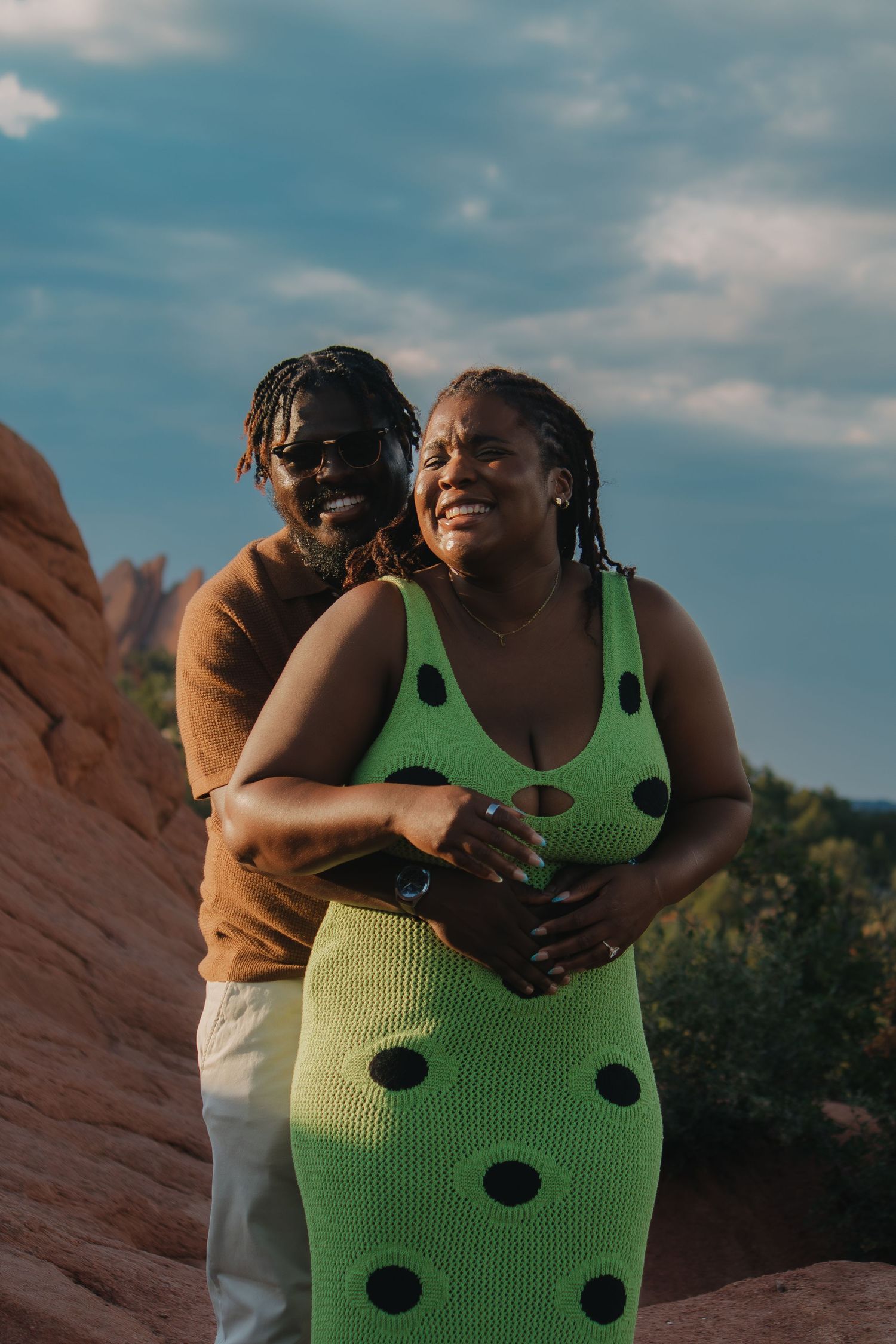 A couple shares an intimate moment outdoors against a backdrop of red rocks and blue sky.
