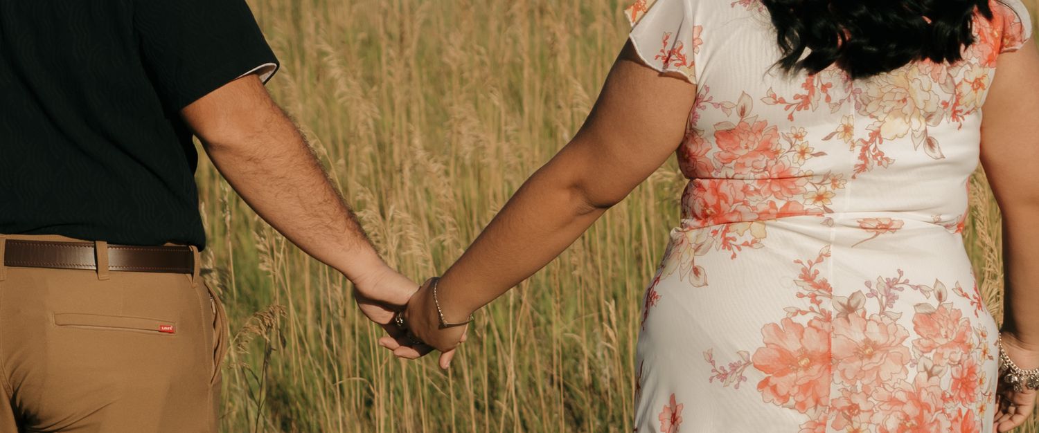 Person in floral dress holding hands with others while standing outdoors in a grassy field at sunset.