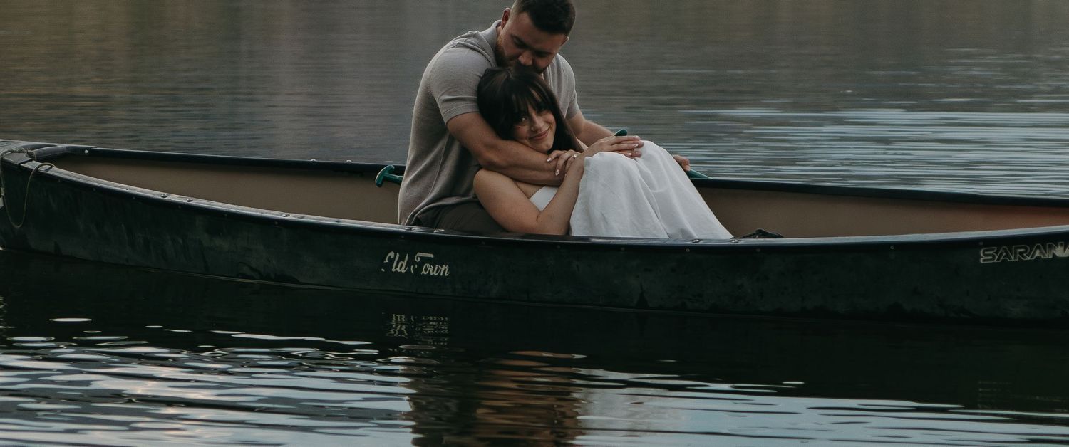 Couple sitting together in a wooden canoe on calm lake waters during sunset.