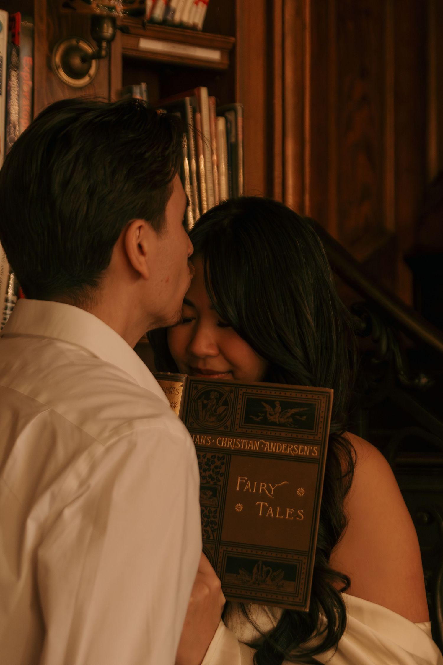 A couple embraces near bookshelves with vintage fairy tale books visible in the background.