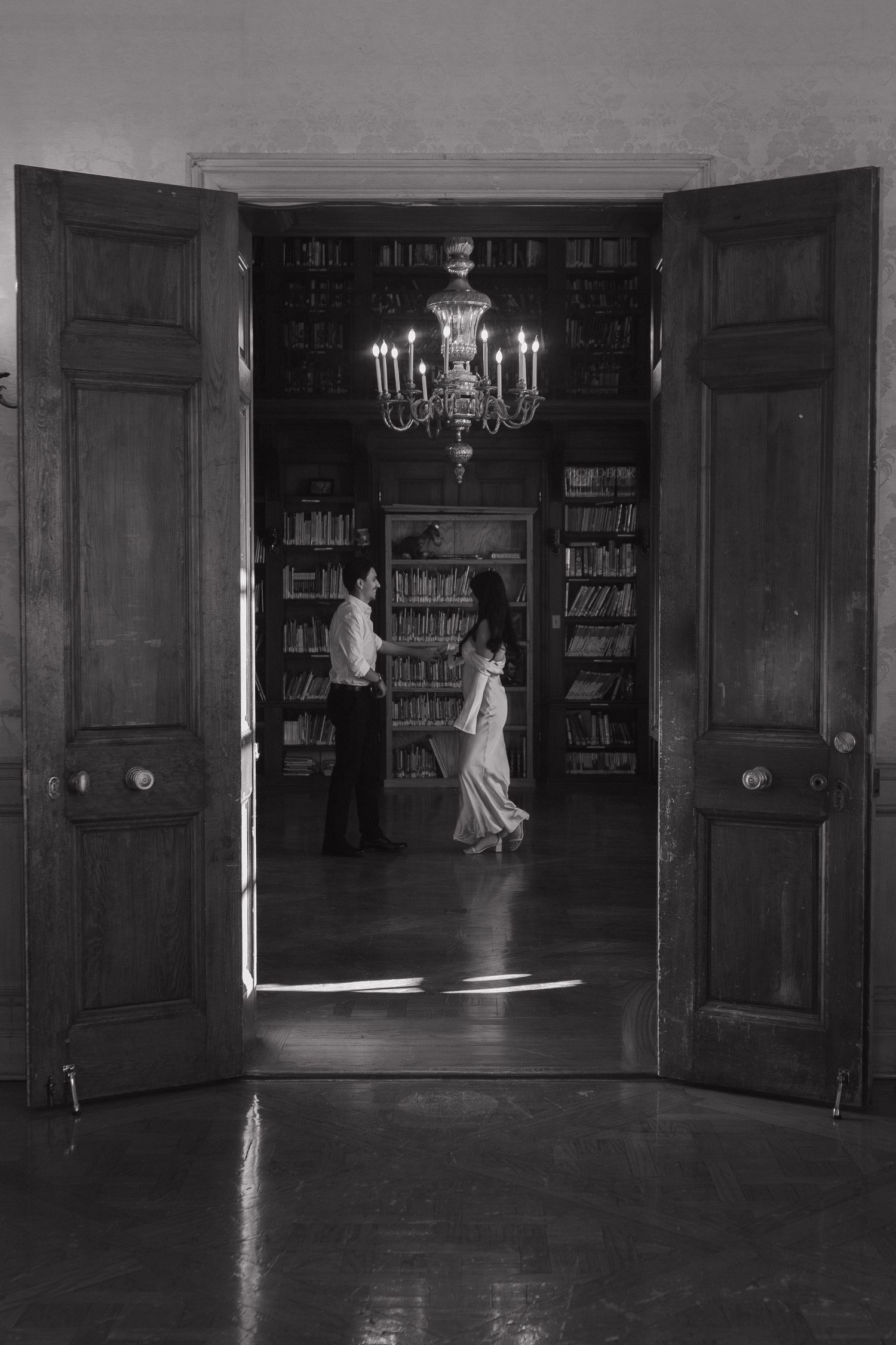 A dimly lit vintage library interior with wooden paneling and chandeliers.
