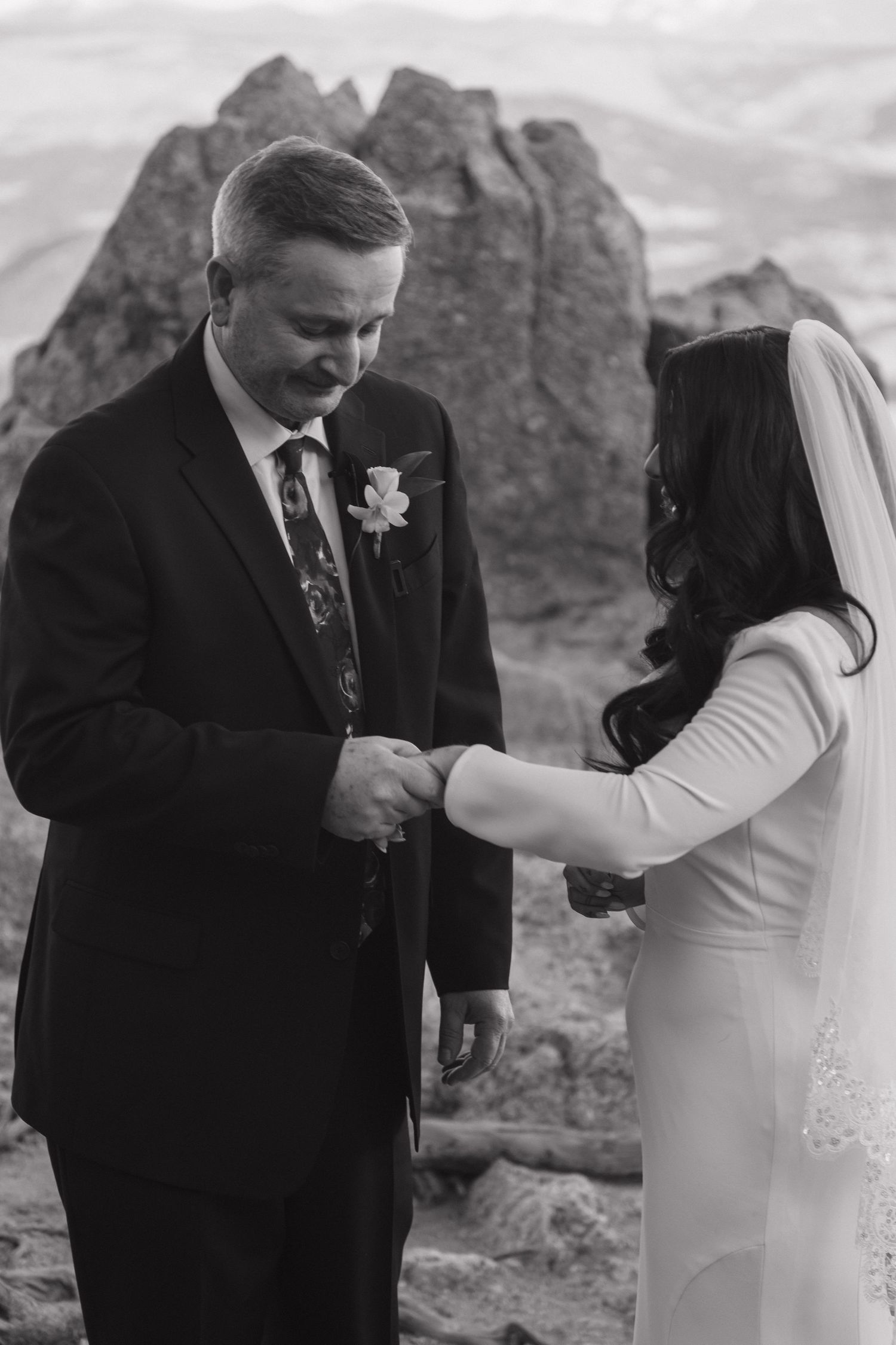 Black and white photo of bride placing ring on grooms finger at mountain ceremony.