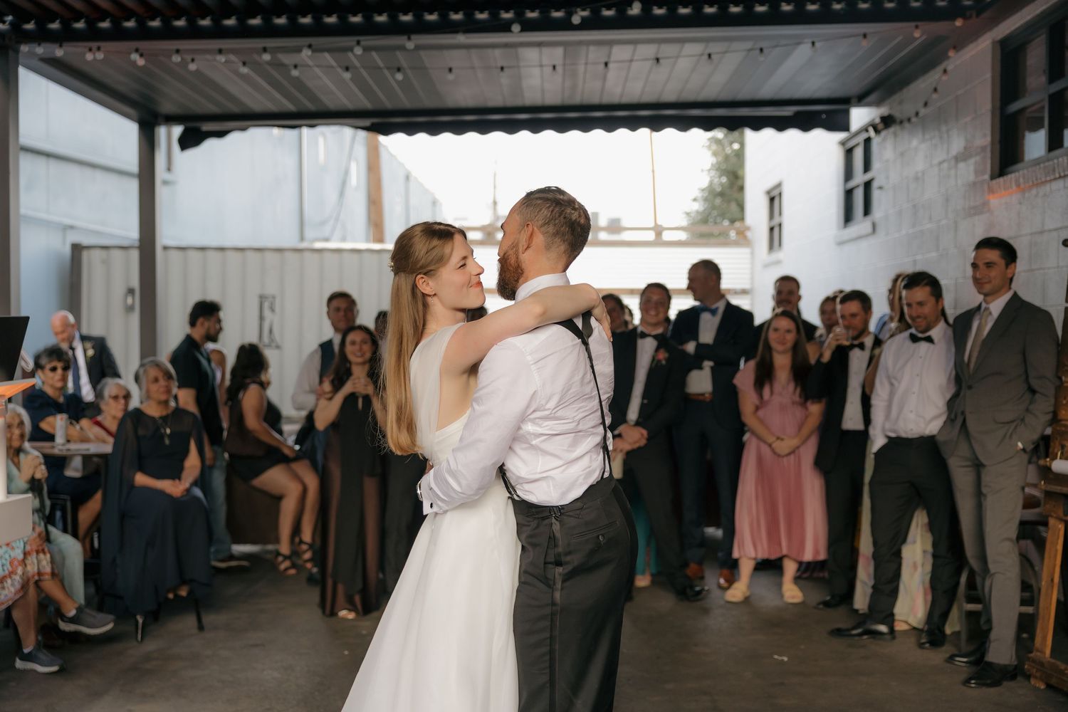 Bride and groom share romantic first dance surrounded by guests at outdoor wedding reception.