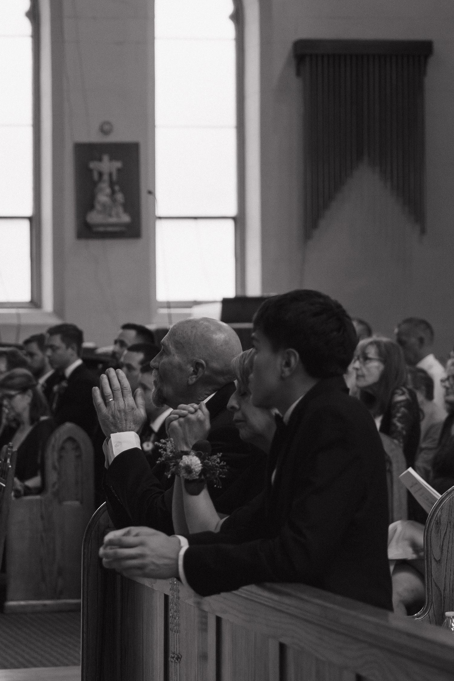 Black and white photo of wedding guests praying in church pews during a ceremony.