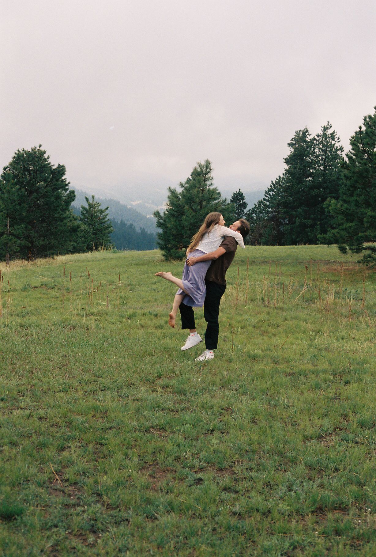 Man lifting woman in his arms in a romantic embrace in a lush green mountain meadow.